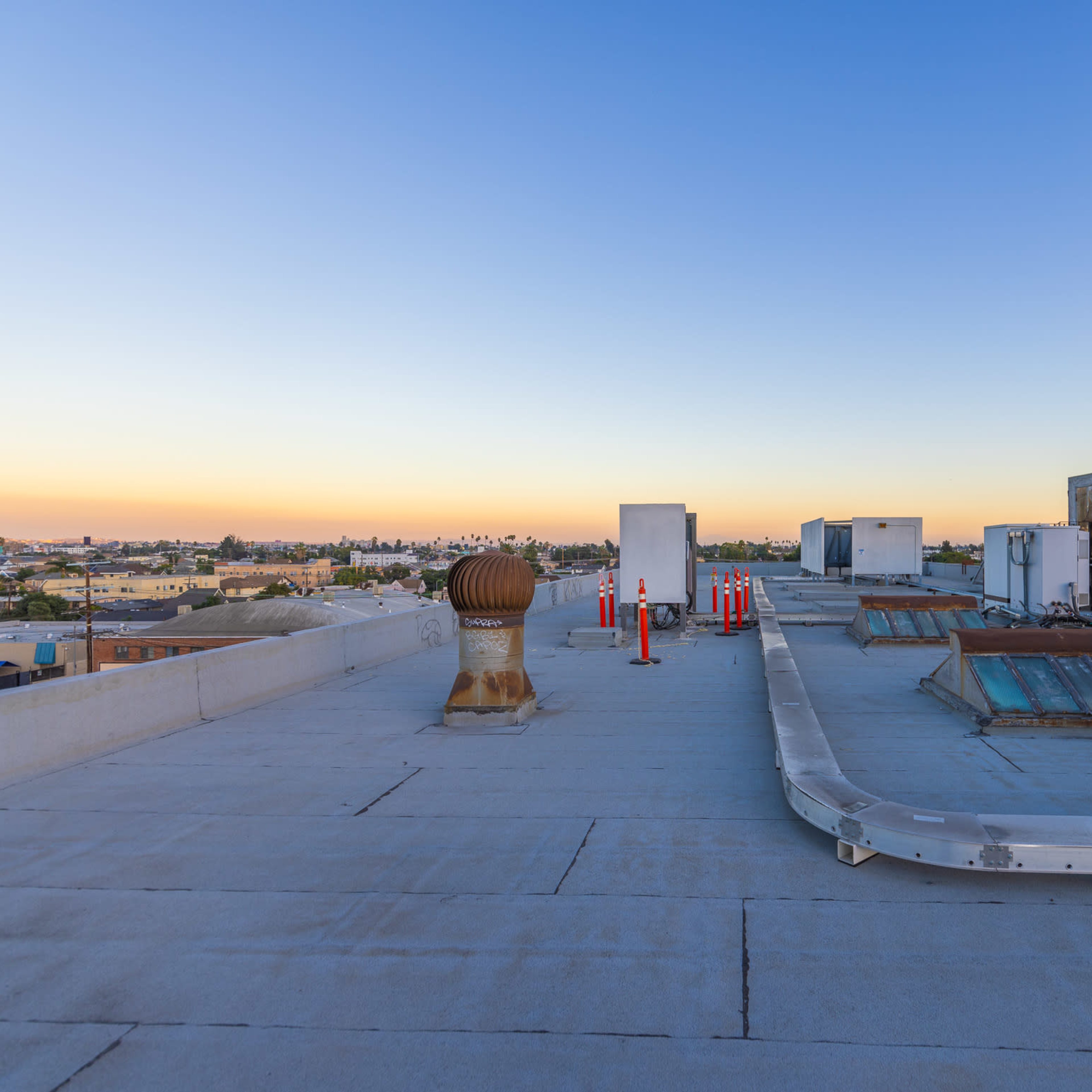 A rooftop scene with ventilation units, pipes, and a clear sky transitioning from blue to orange at sunset.