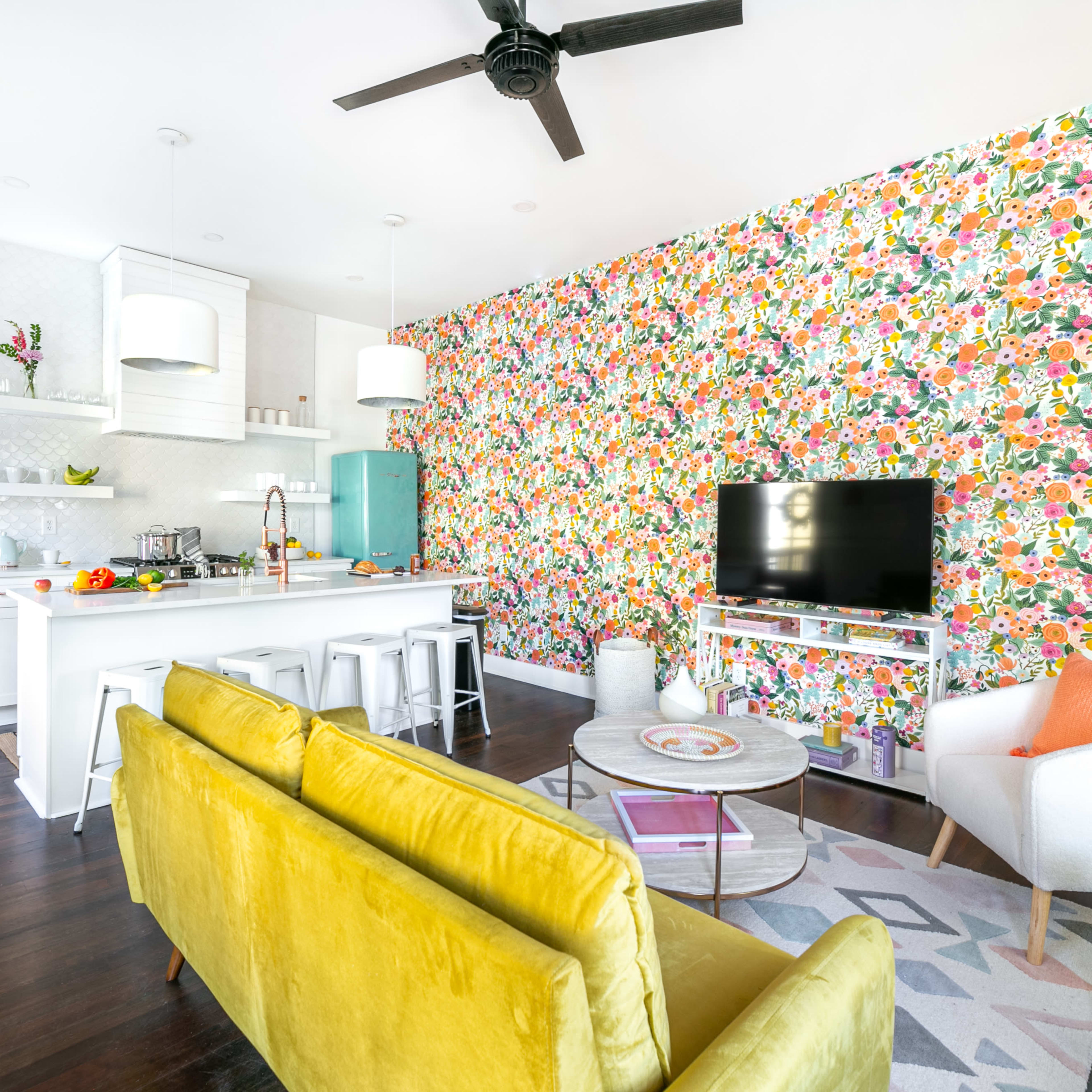 A modern living space with a vibrant floral wallpaper, a kitchen island with bar stools, a TV area, and a mix of contemporary furniture.