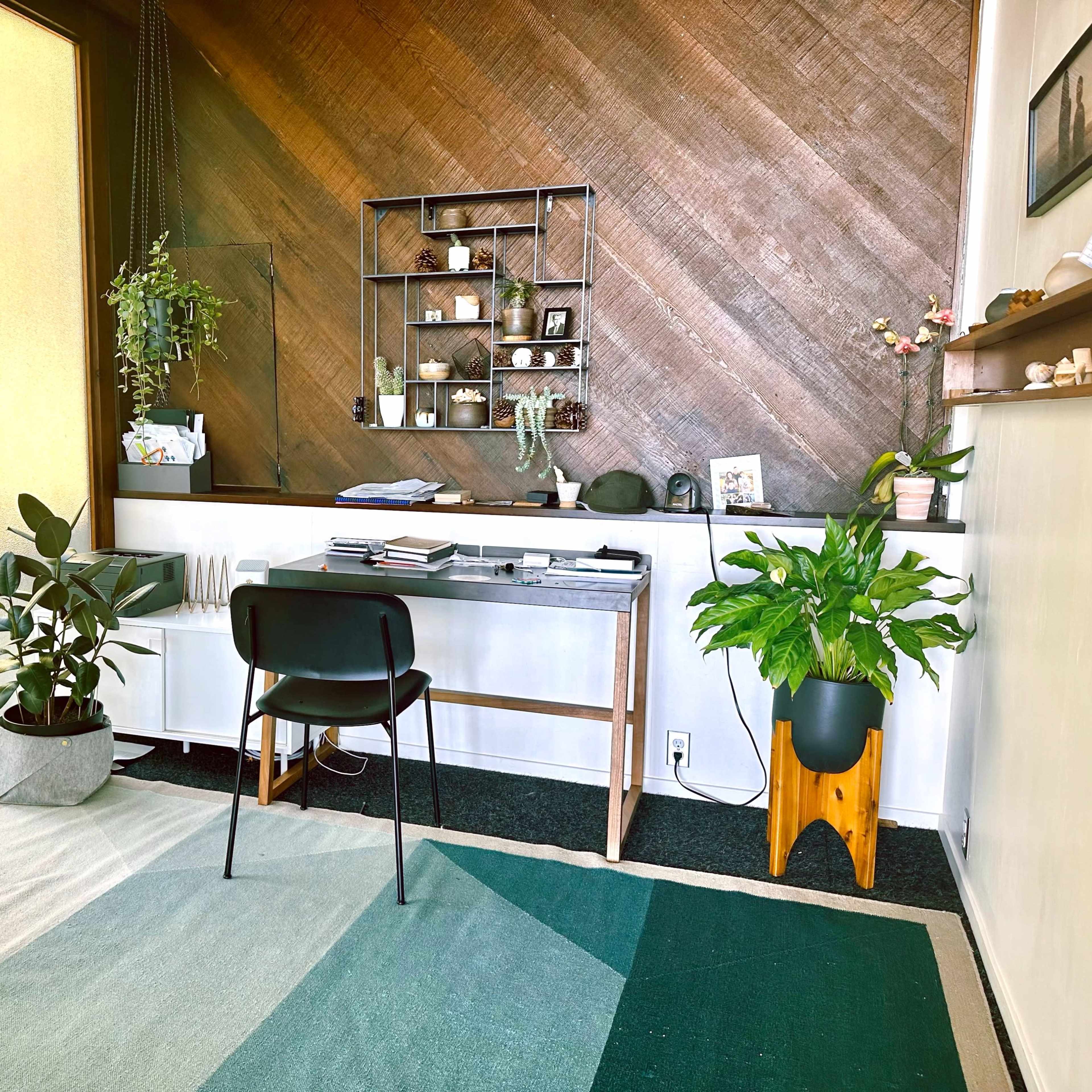 A modern workspace featuring a desk with neatly arranged items, plants, and a wall with a textured design.