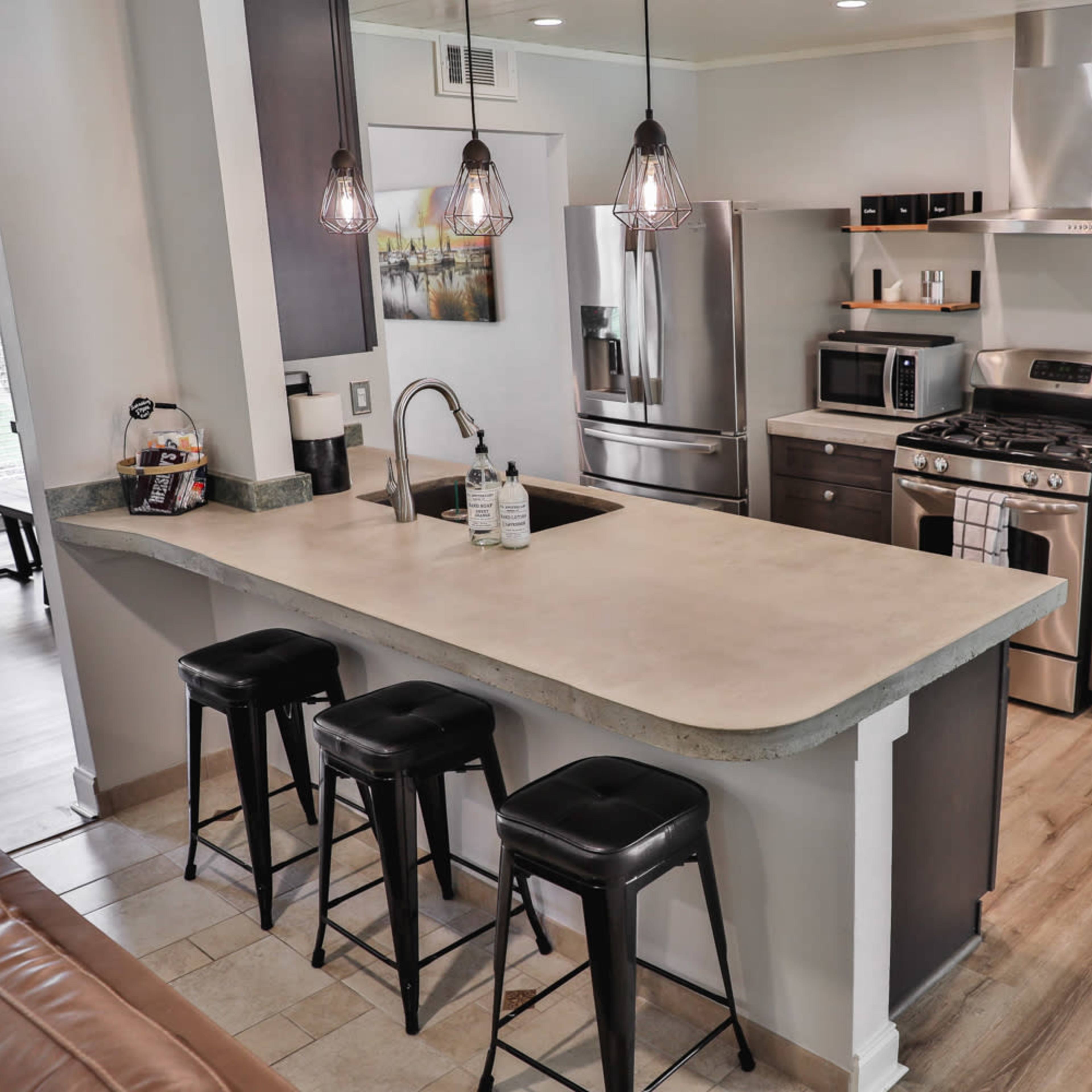 A modern kitchen with stainless steel appliances, a central island with seating, and wood laminate flooring.