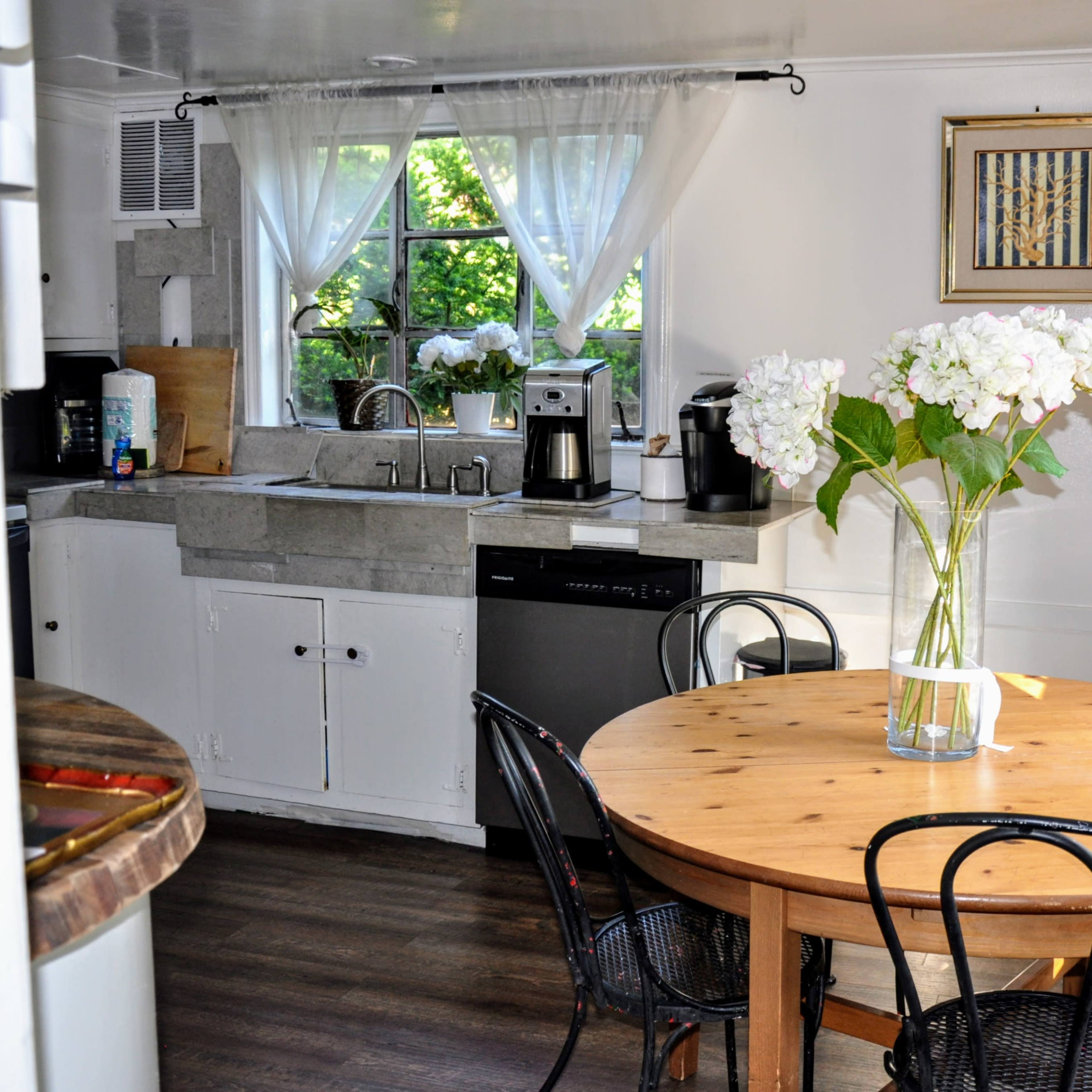 A kitchen with a round wooden table and chairs, featuring a vase of flowers on the table and appliances along the walls.