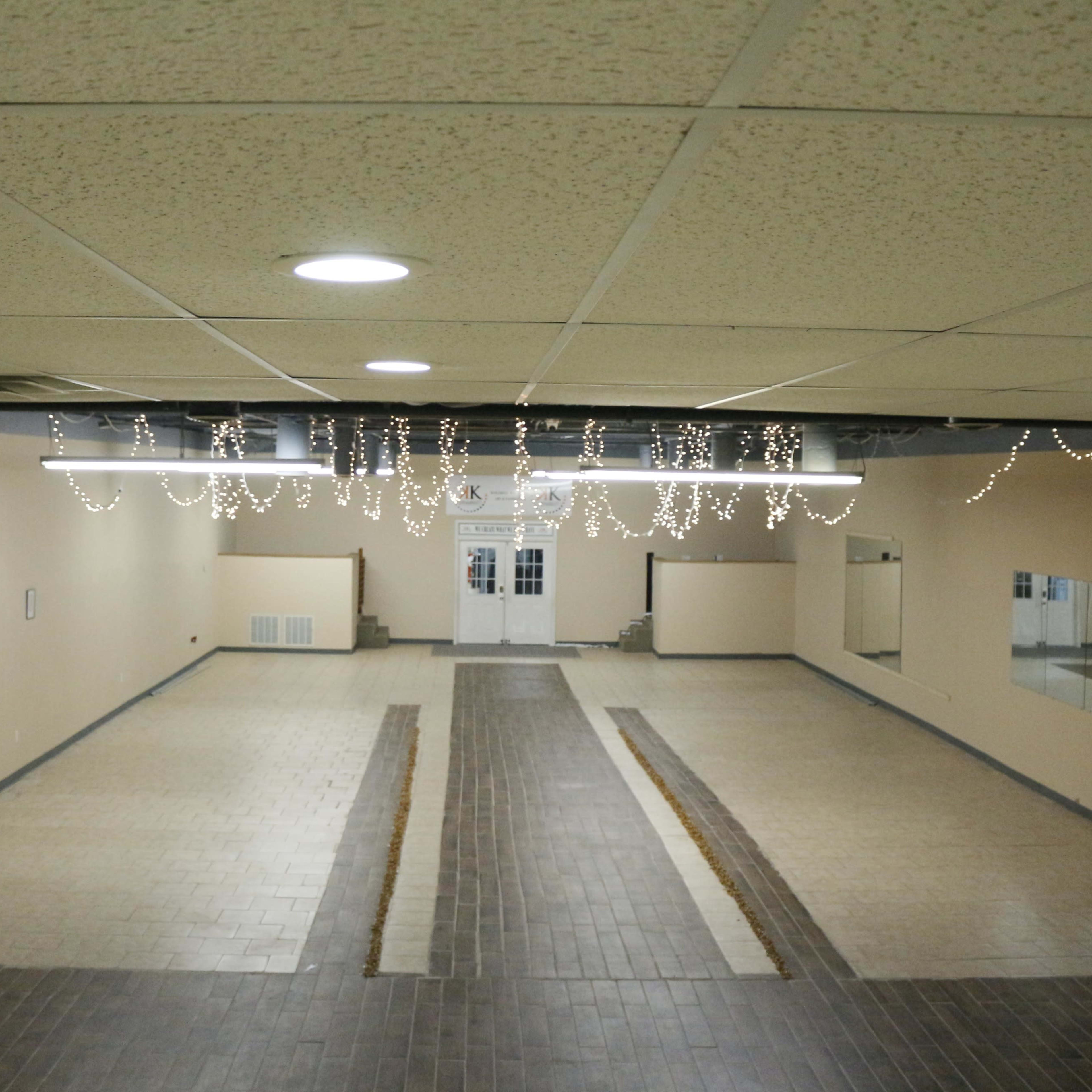 A spacious, empty interior room with tile flooring, featuring hanging decorative lights and multiple mirrors along the walls.