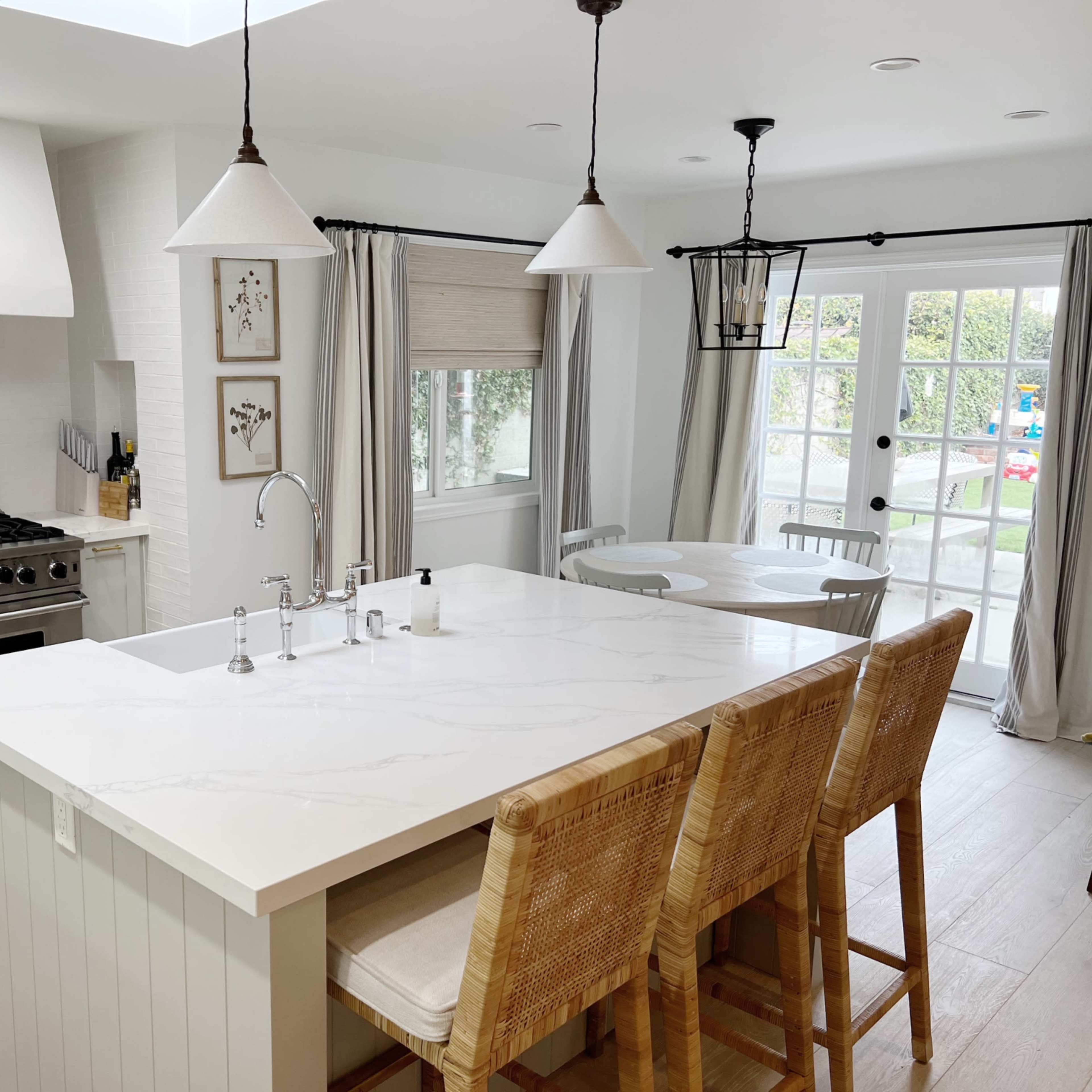 A modern kitchen with a large island, bar stools, stainless steel appliances, and a dining area that opens to a patio through double doors.