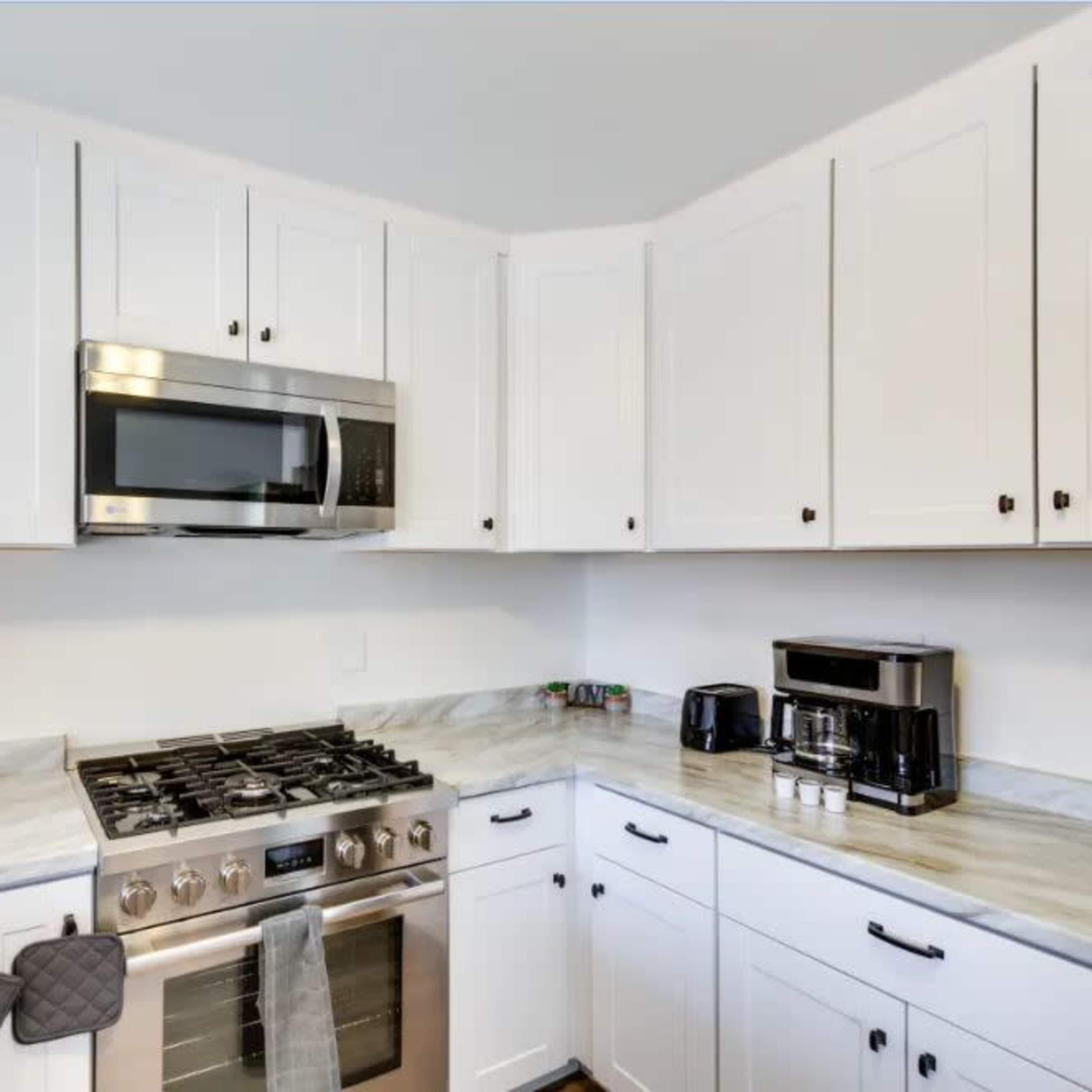 A modern kitchen features white cabinetry, stainless steel appliances, and a marble countertop.