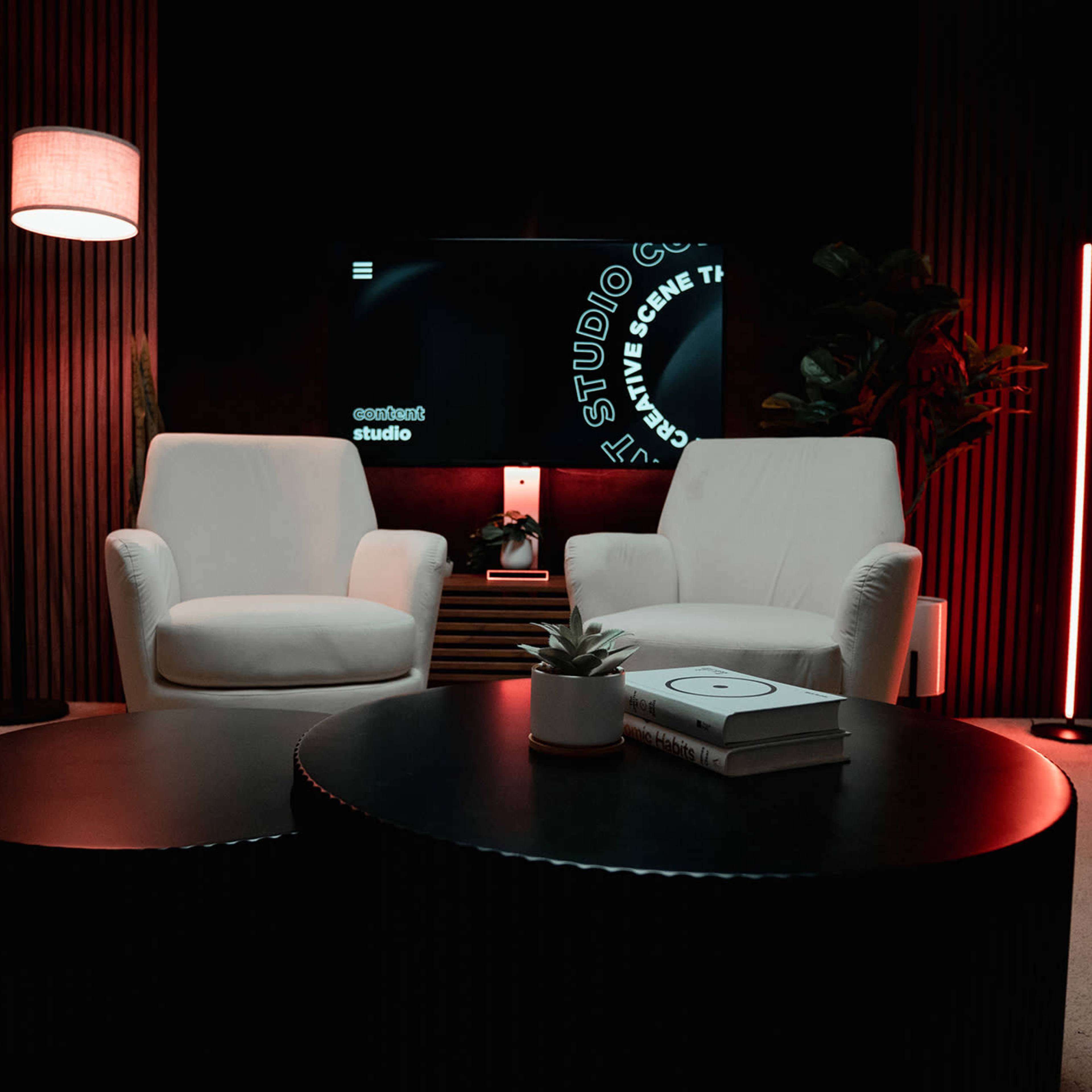 A modern living space with two white armchairs, a dark coffee table, a glowing floor lamp, and a television displaying design elements against a black backdrop.