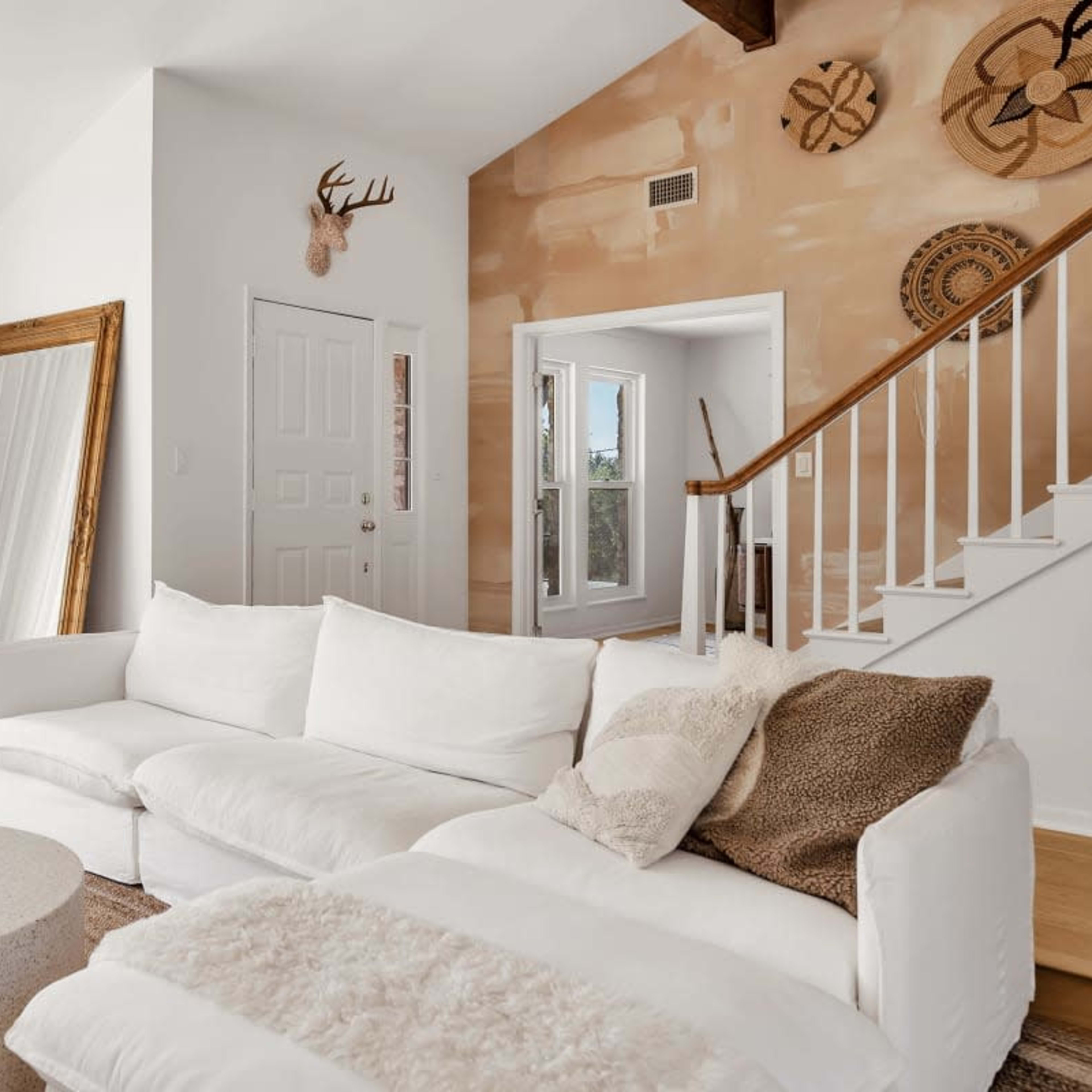 A bright, modern living room featuring a white sectional sofa, a round coffee table, large windows, and decorative wall elements.