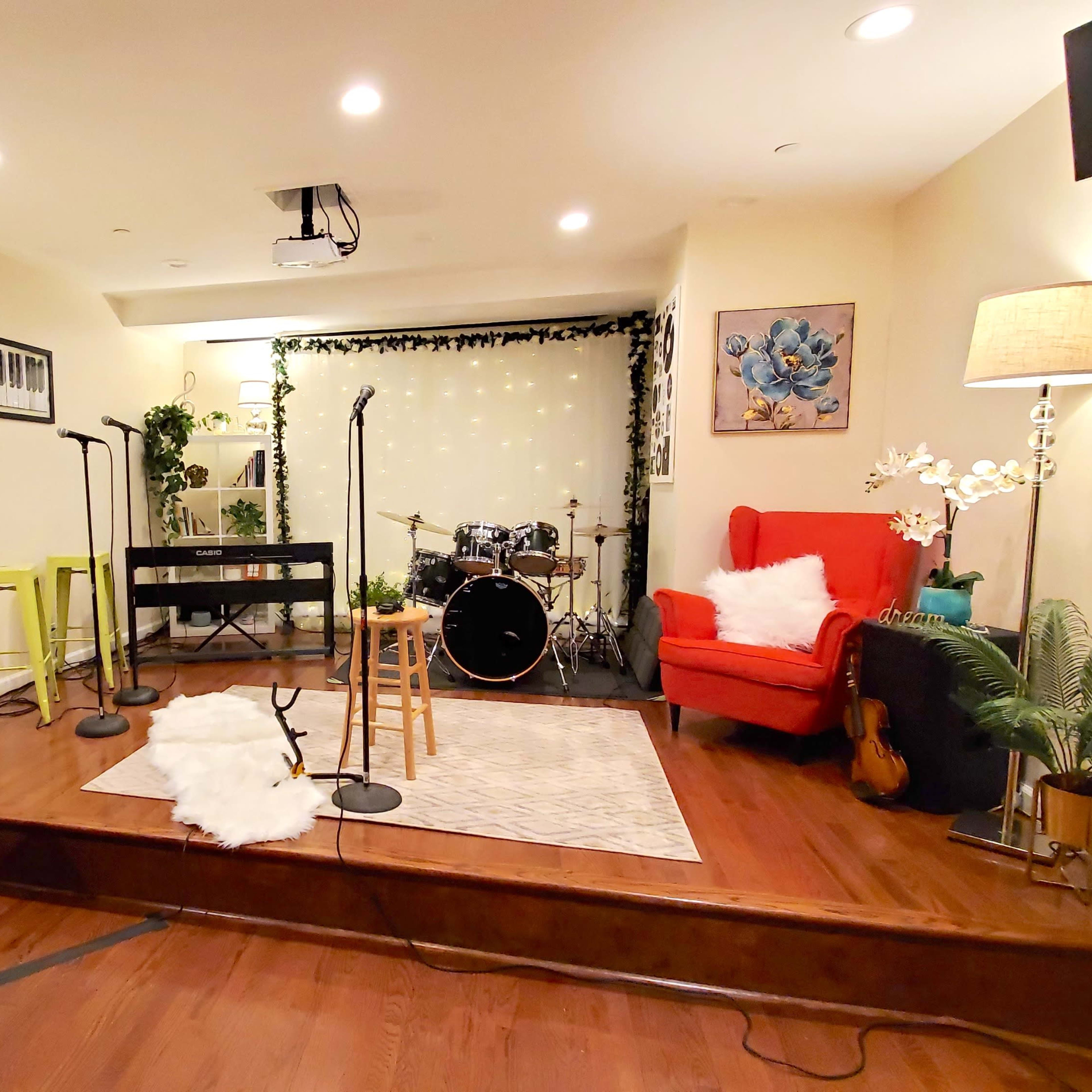 A performance space features musical instruments, microphones, and comfortable seating against a backdrop of decorative plants and ambient lighting.