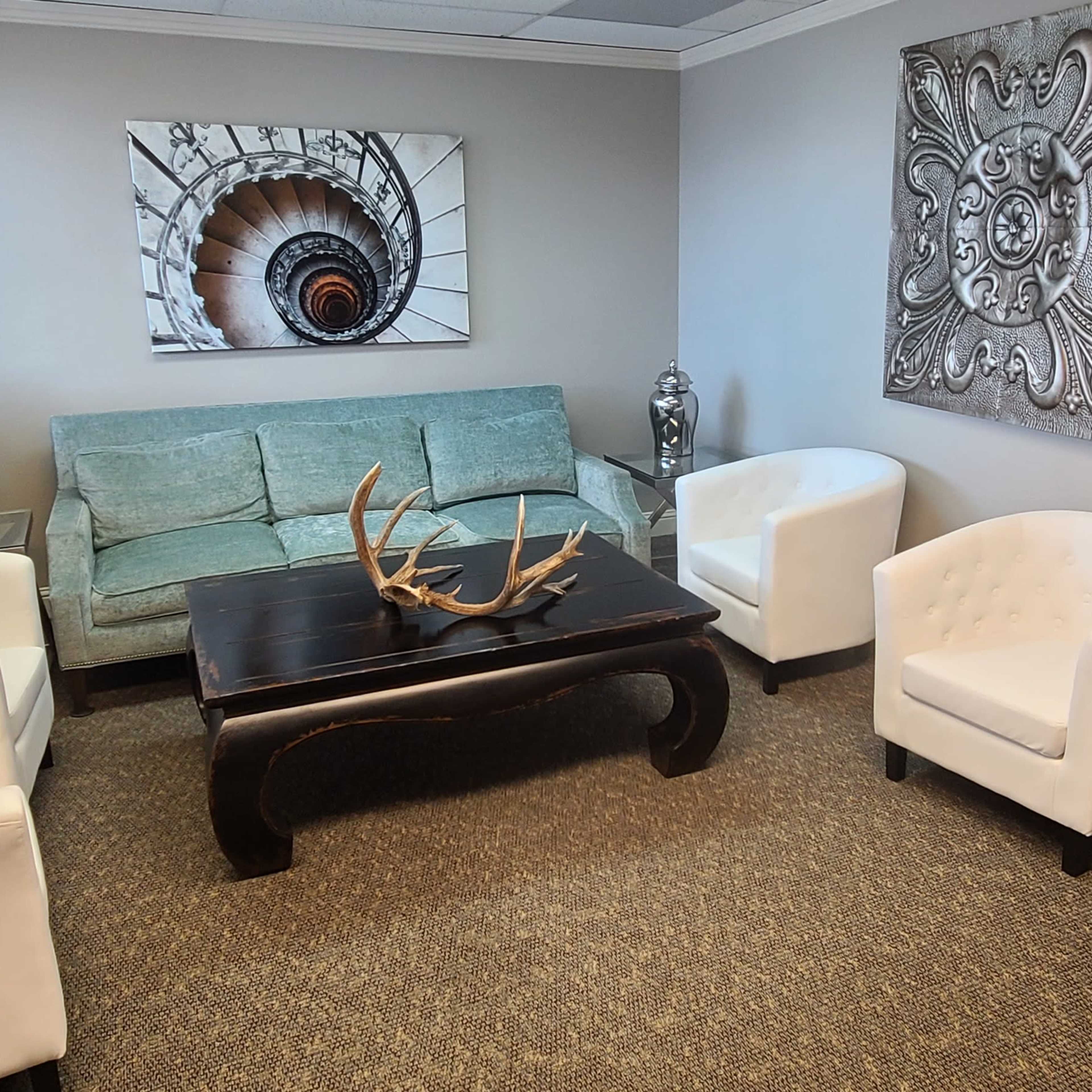 The room features a green sofa and two white armchairs arranged around a dark coffee table, with decorative art on the walls and a television in one corner.