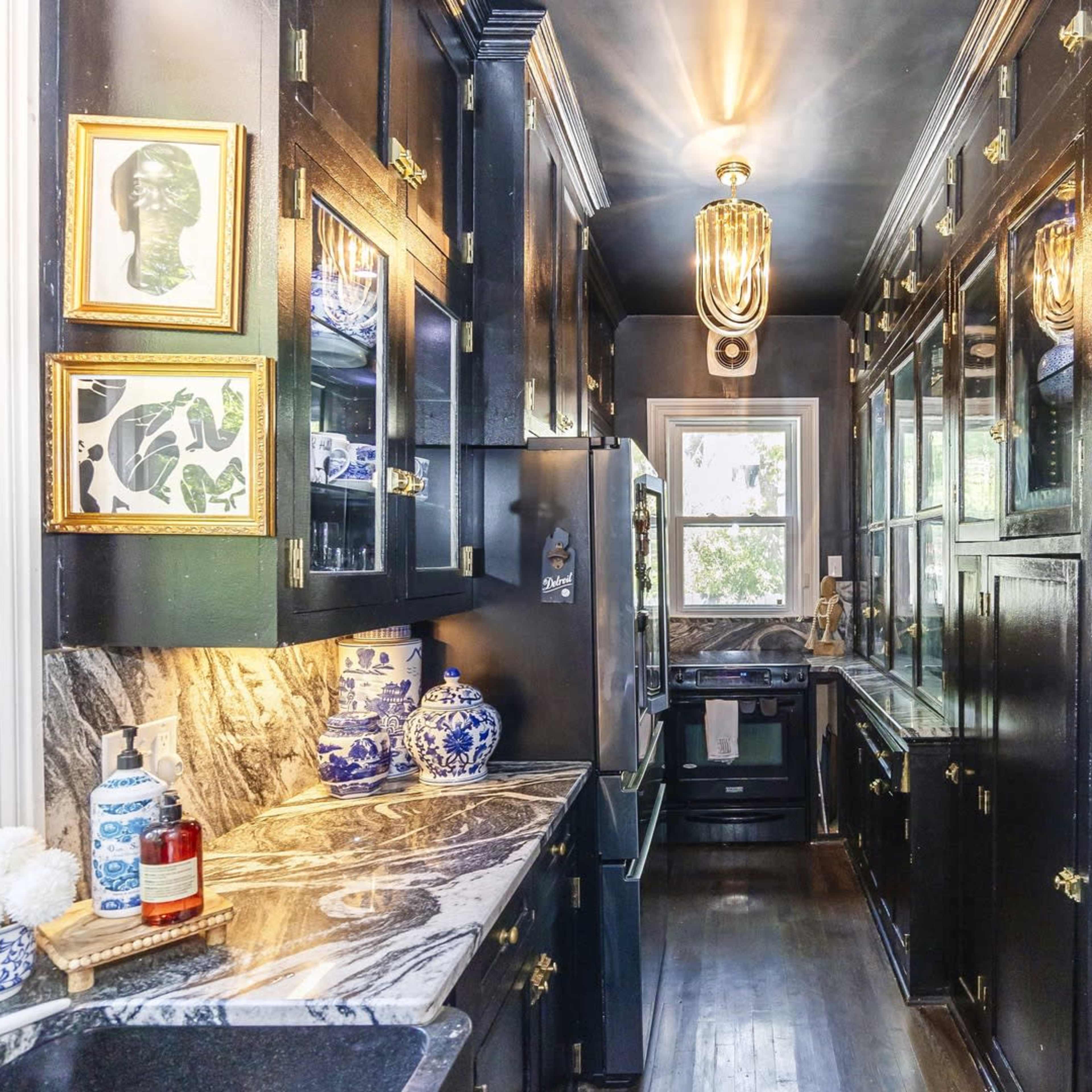 A narrow kitchen features black cabinetry, marble countertops, and decorative blue and white ceramics along with a window that lets in natural light.