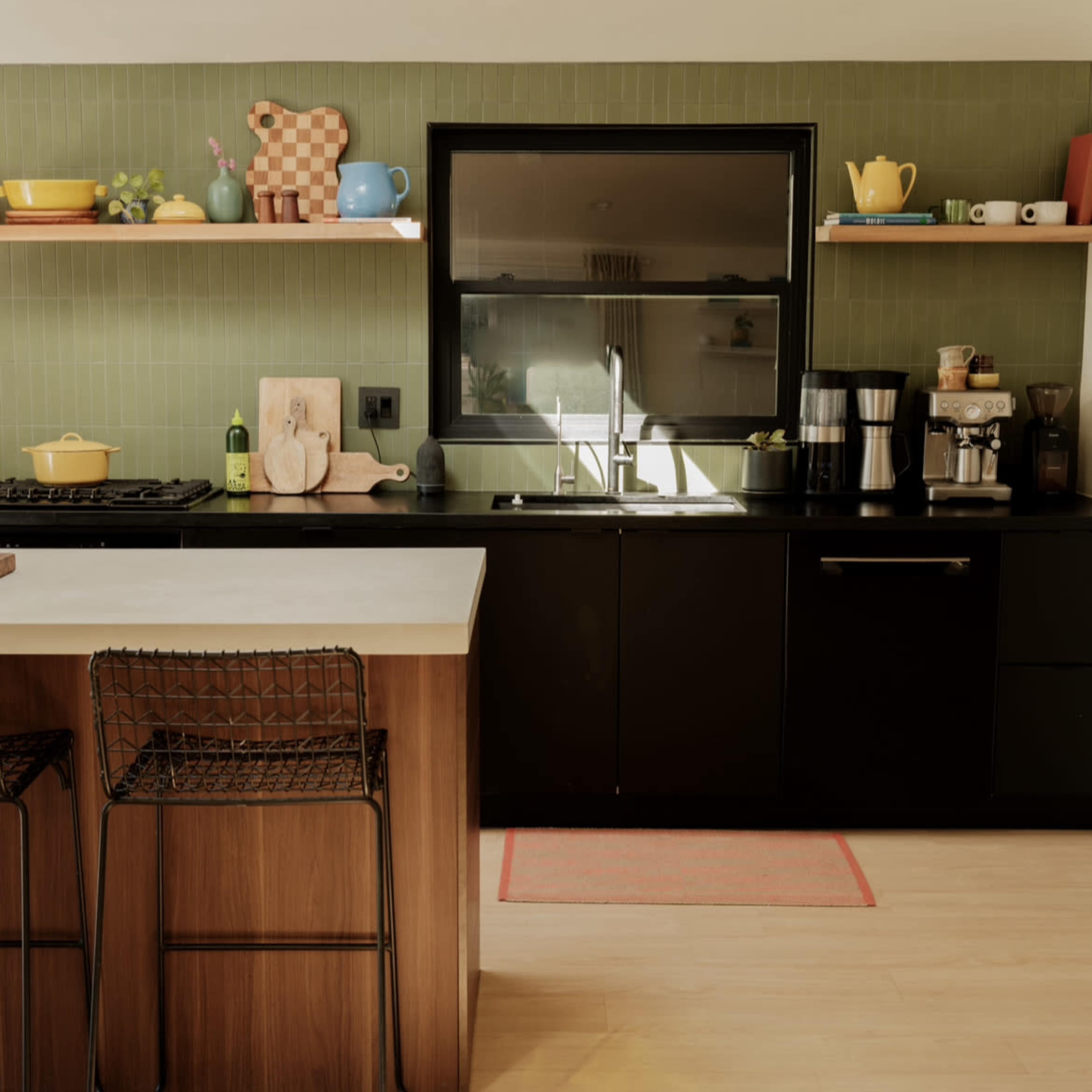 A modern kitchen features a black countertop, wooden bar stools, and a variety of colorful kitchenware displayed on shelves.