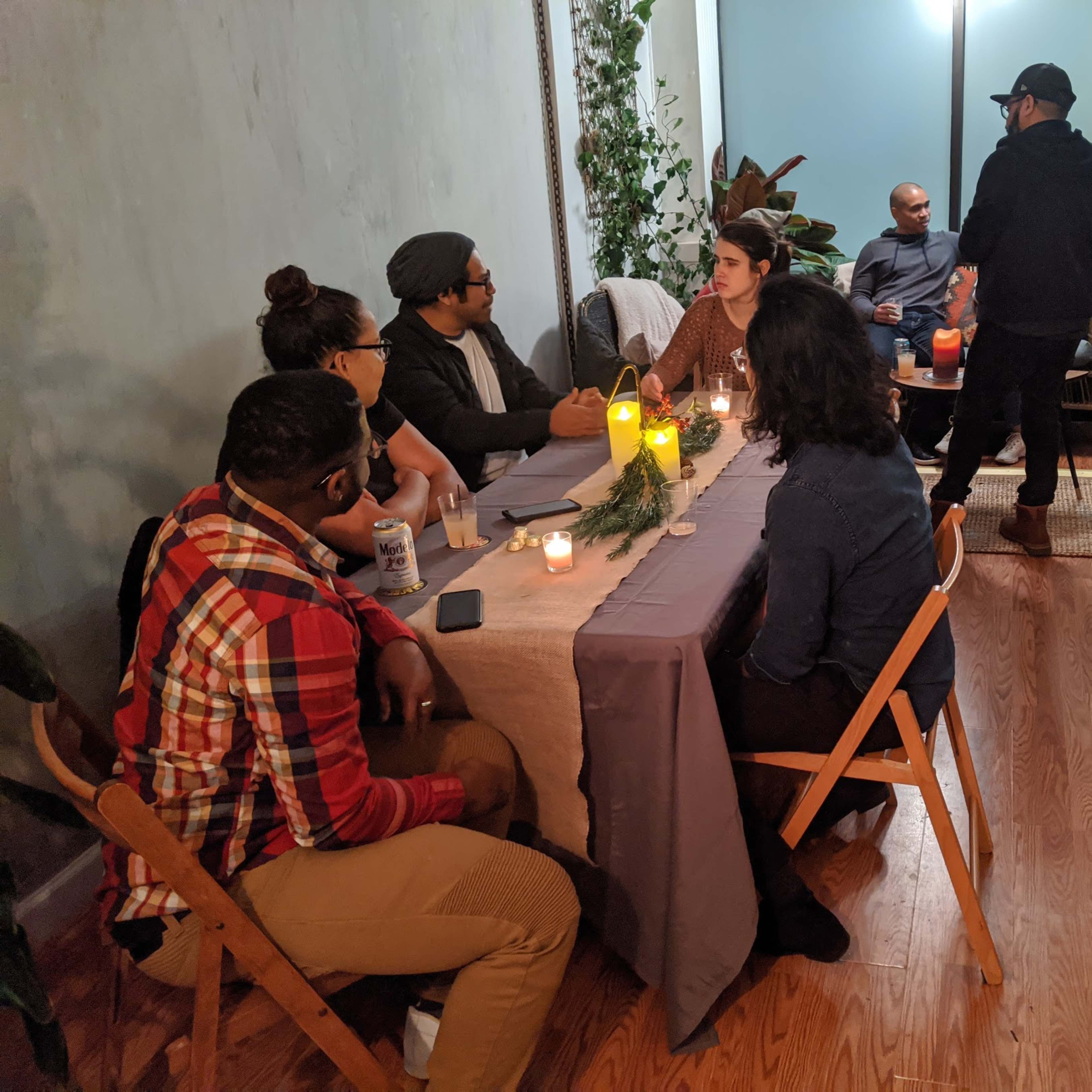 A group of people sits around a table adorned with candles and greenery in a well-decorated indoor space.