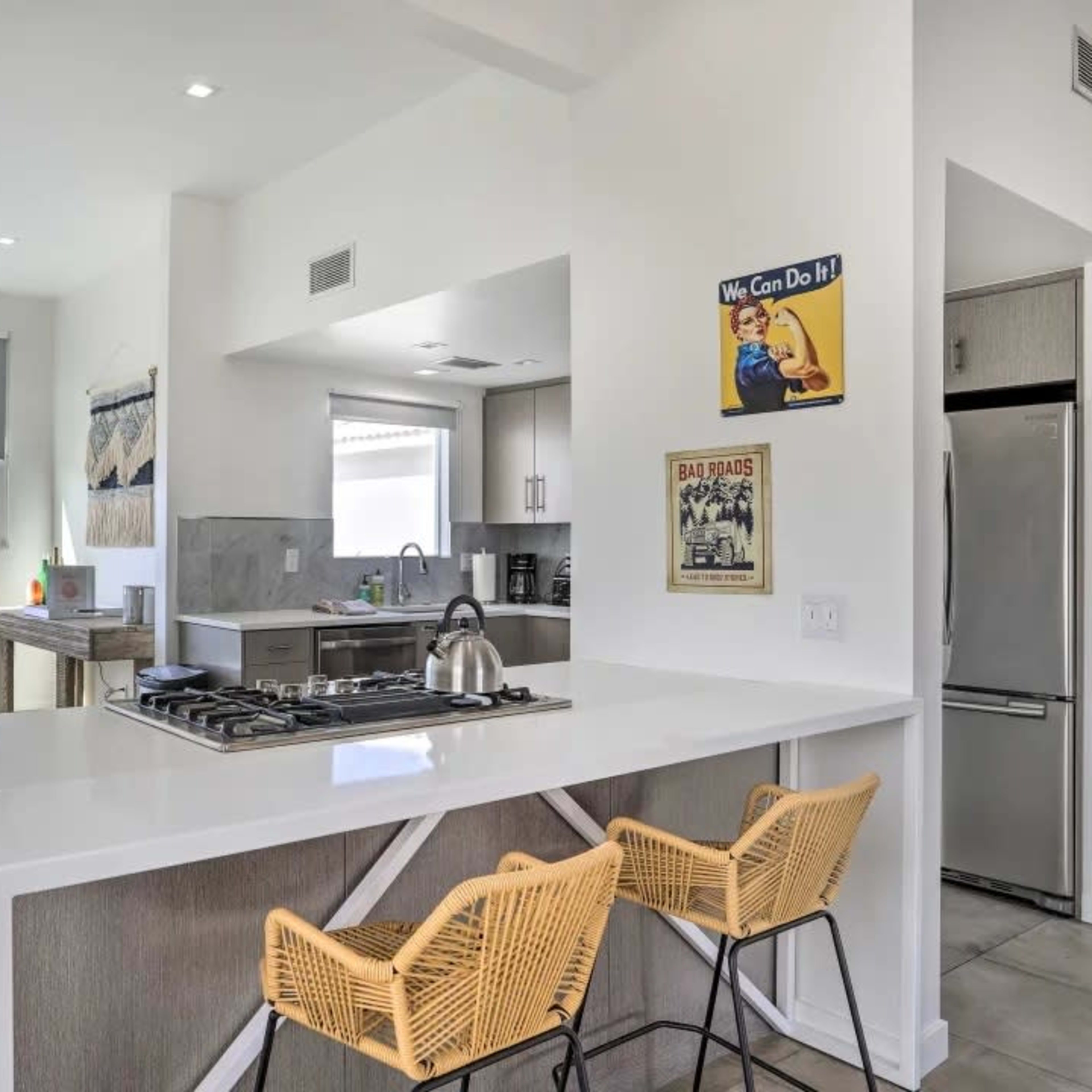A modern kitchen features a gas stove island with bar stools and a dining area with a table overlooking a view outside.