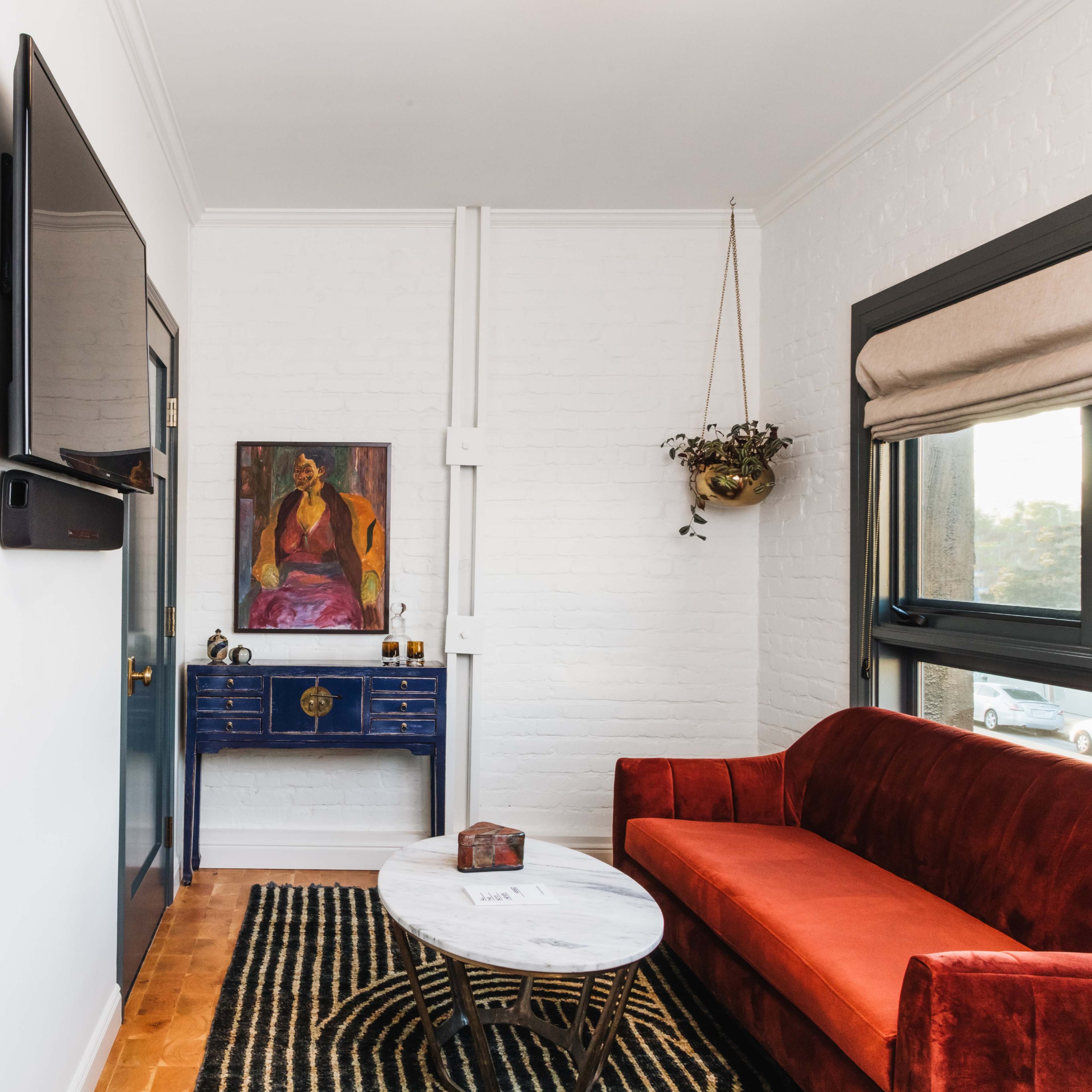 A cozy living space featuring a red velvet couch, a marble coffee table, and a wall-mounted television, accompanied by an art piece and decorative elements.