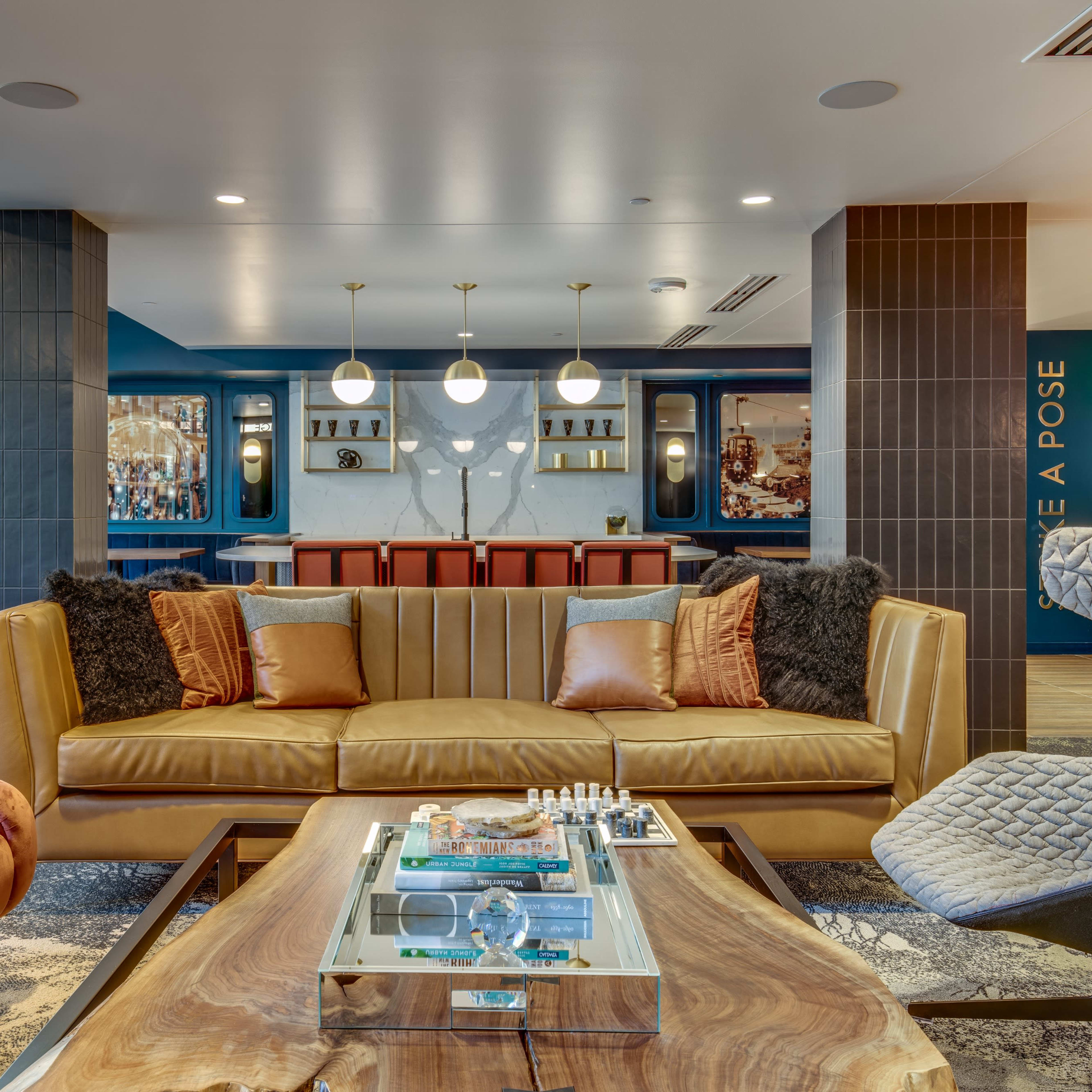 A modern lobby area featuring a yellow couch, two accent chairs, a coffee table with a chess set, and a bar in the background.