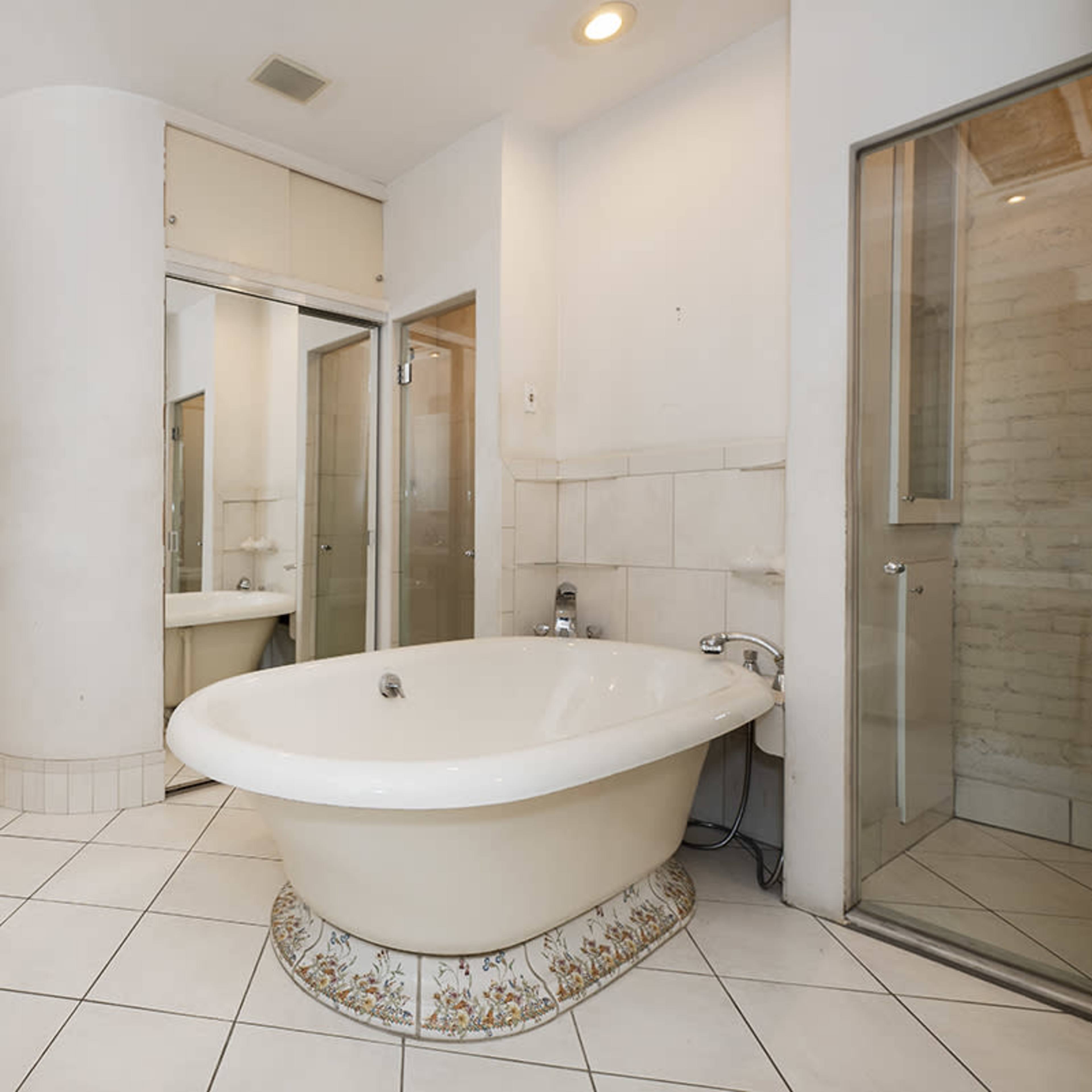A bathroom features a freestanding bathtub, a glass shower enclosure, and dual sinks, all surrounded by tiled walls and floors.