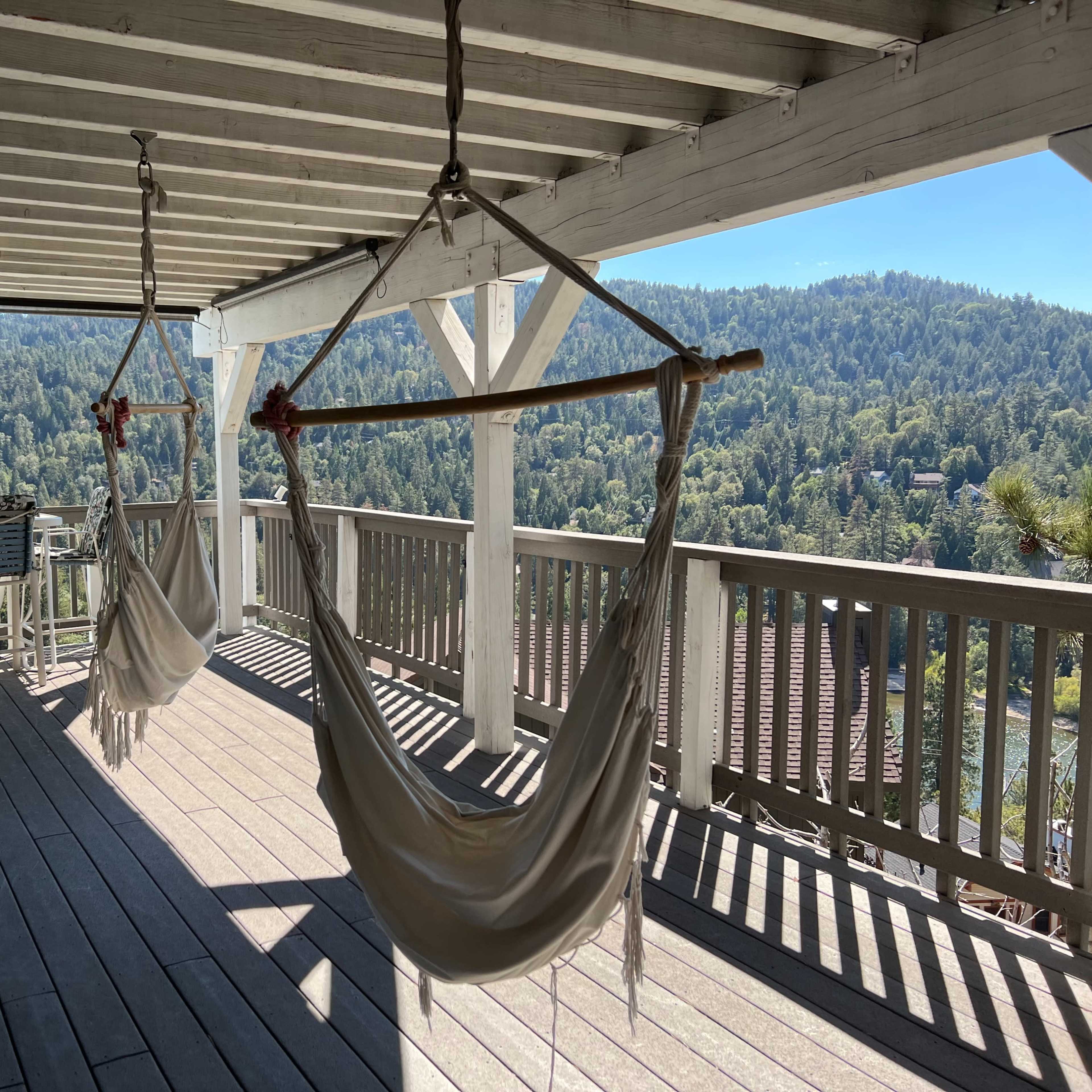 Two hammocks suspended on a wooden deck, overlooking a lush green landscape with mountains in the background.