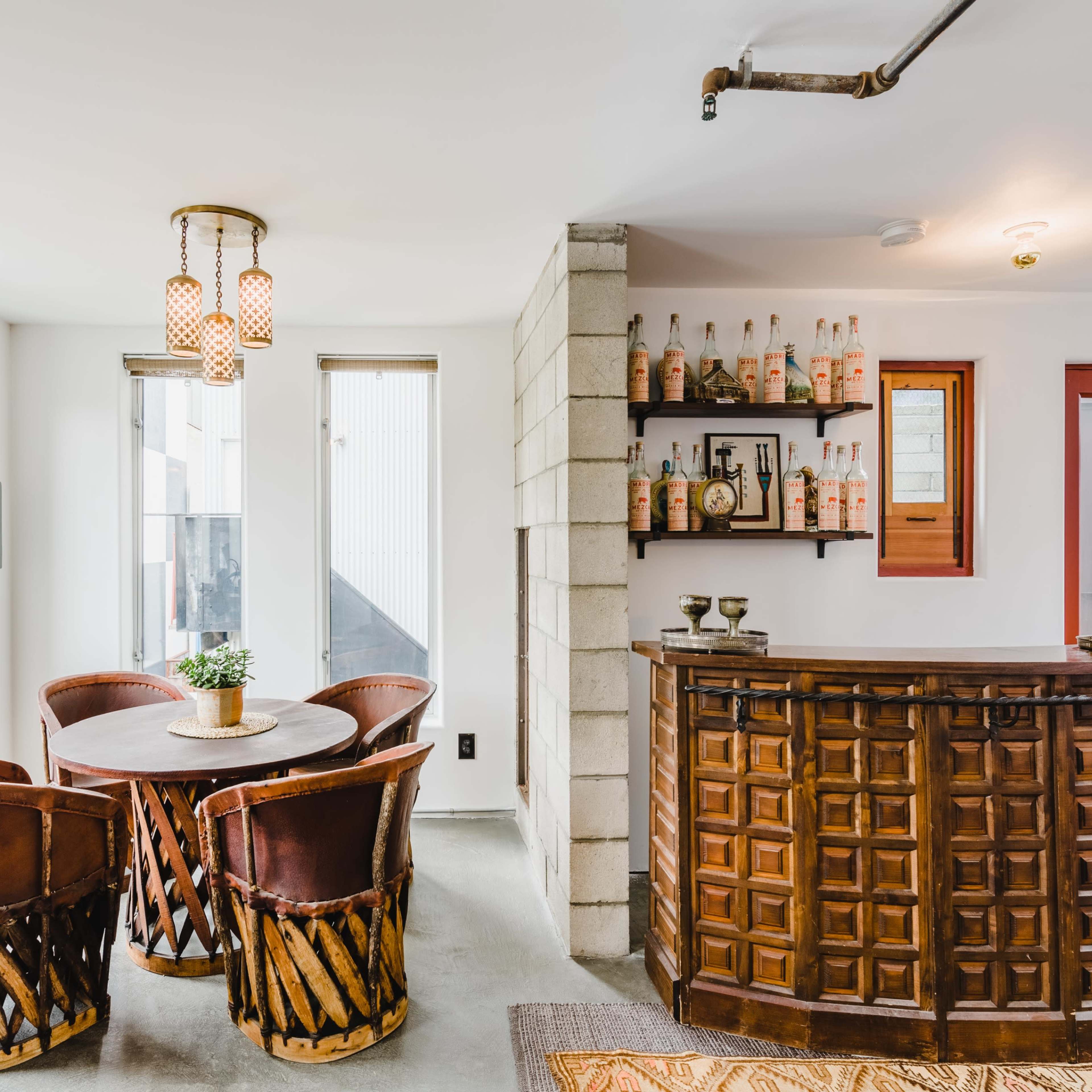 A modern interior with a wooden reception desk, a small round dining table surrounded by four leather chairs, and shelves displaying bottles and decorative items.