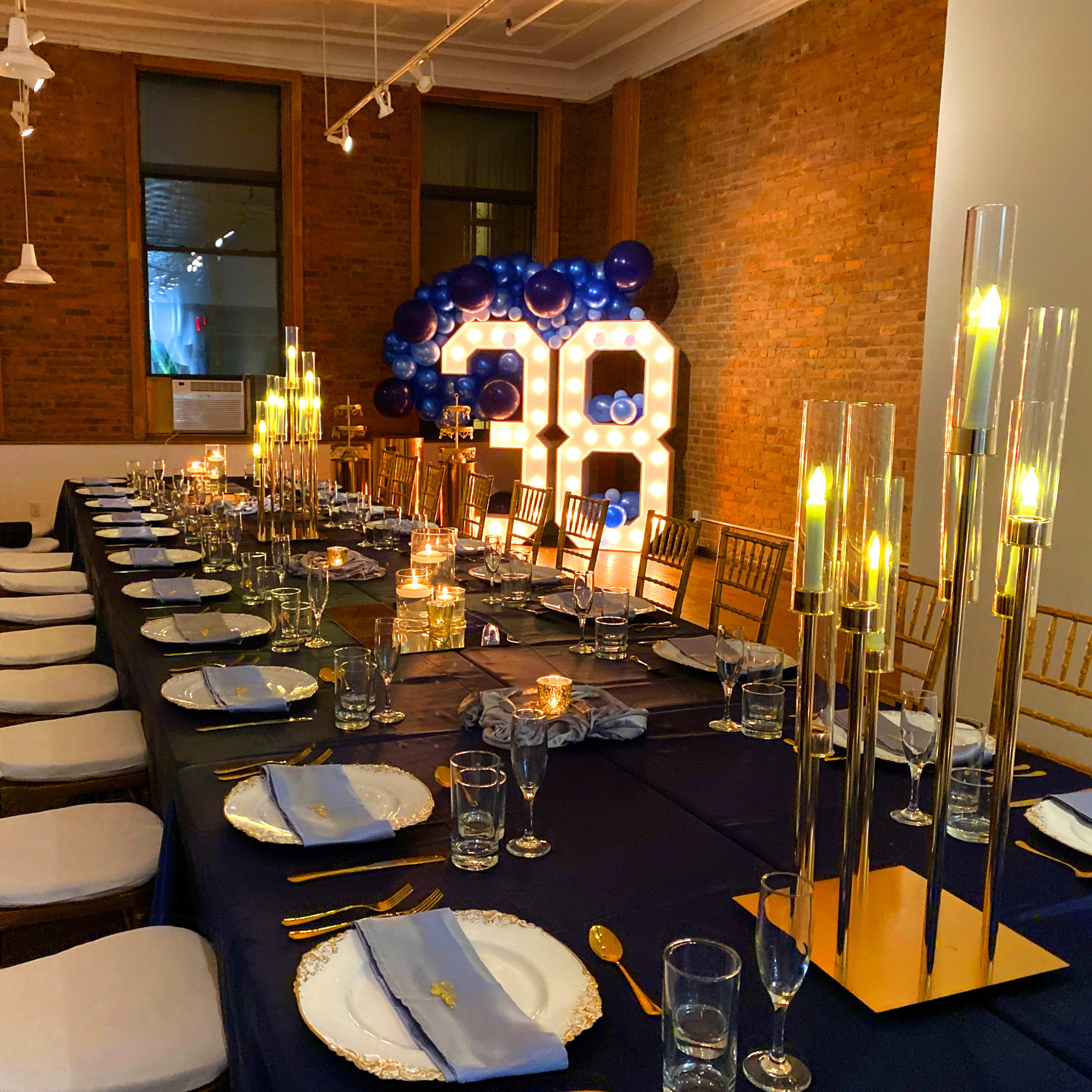 A long dining table is elegantly set for a celebration, complete with candles, glassware, and gold-accented décor, with a large illuminated "30" display in the background.