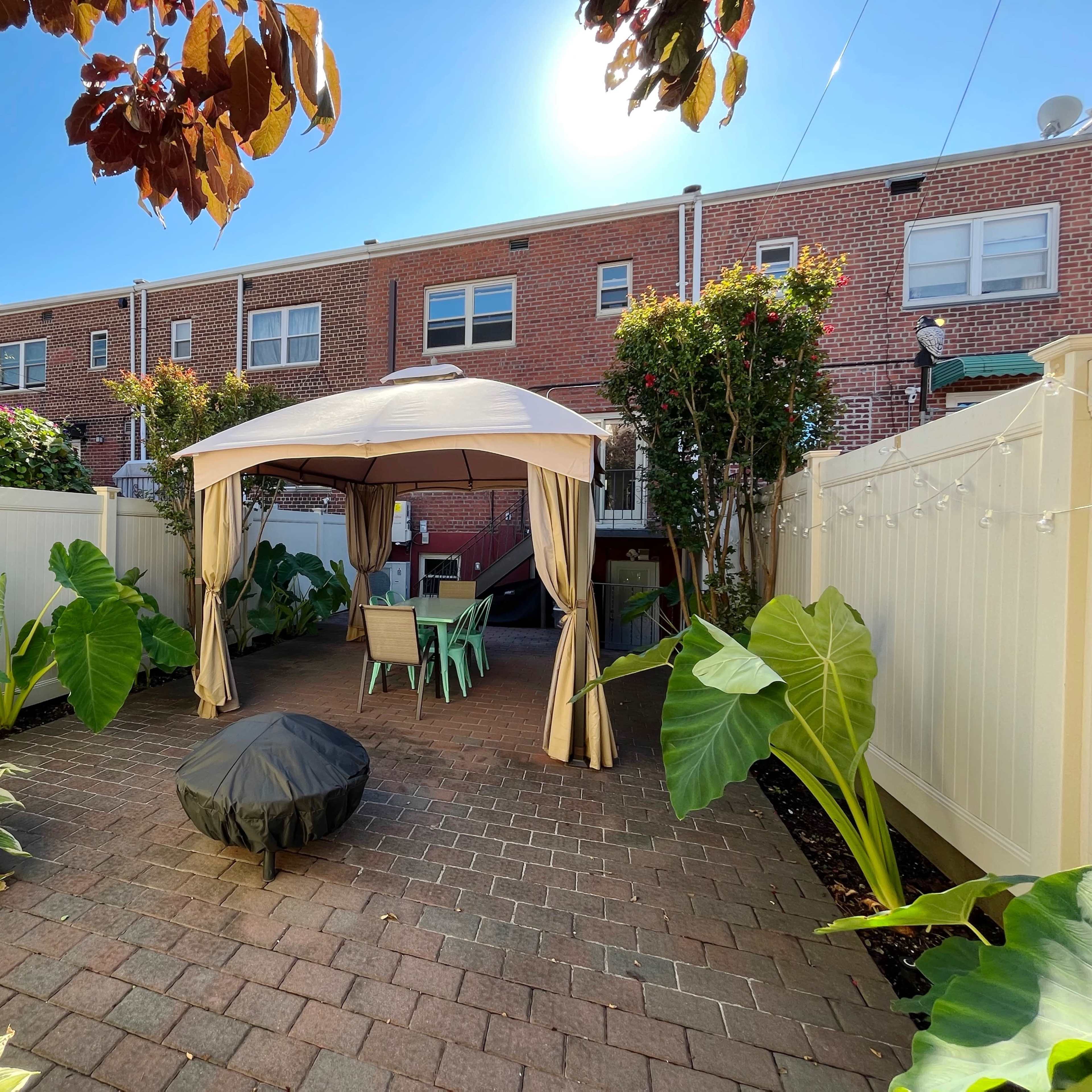 A landscaped backyard with a gazebo surrounded by potted plants and a brick patio.
