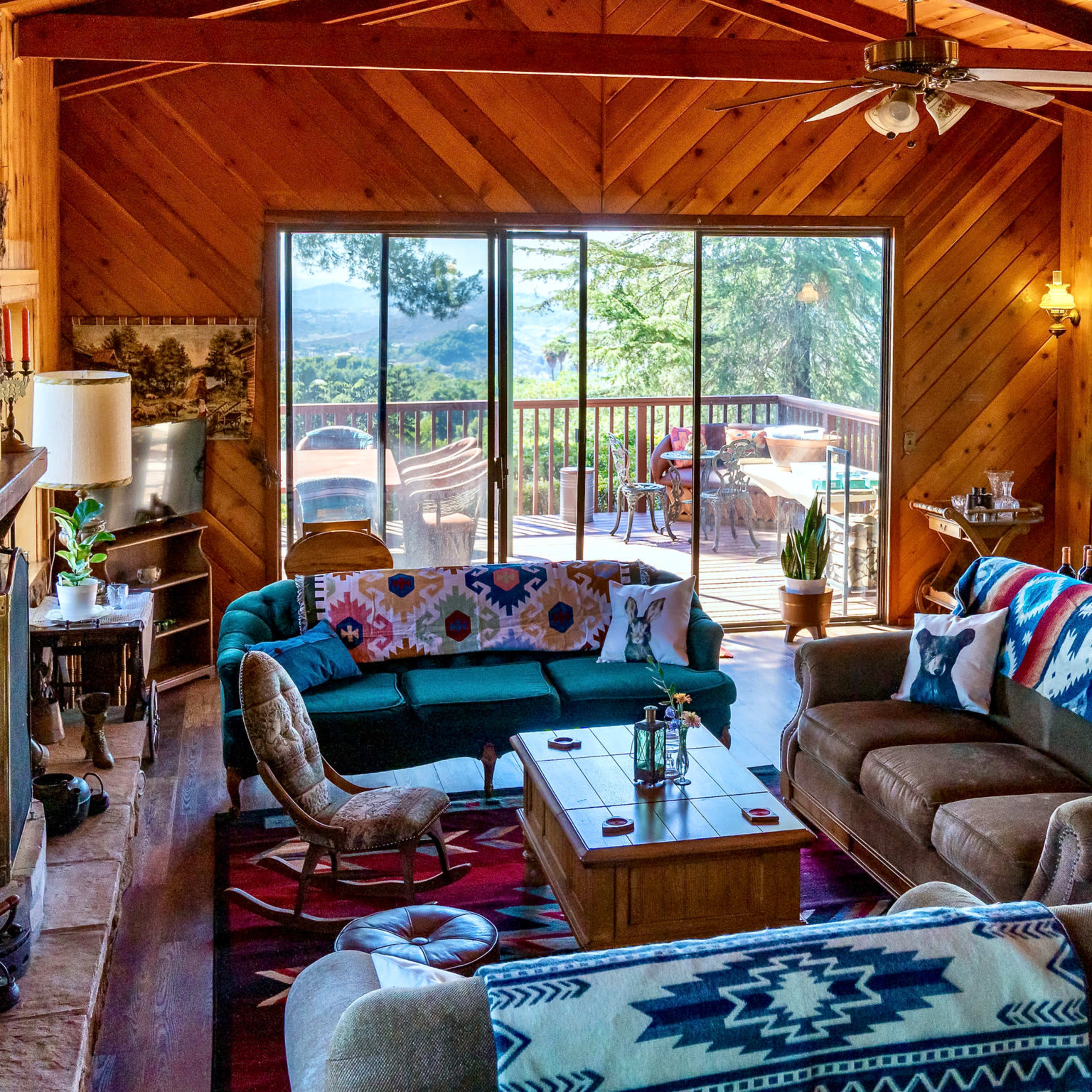 The spacious living room features wooden walls and a large window that opens to a deck overlooking a scenic view.
