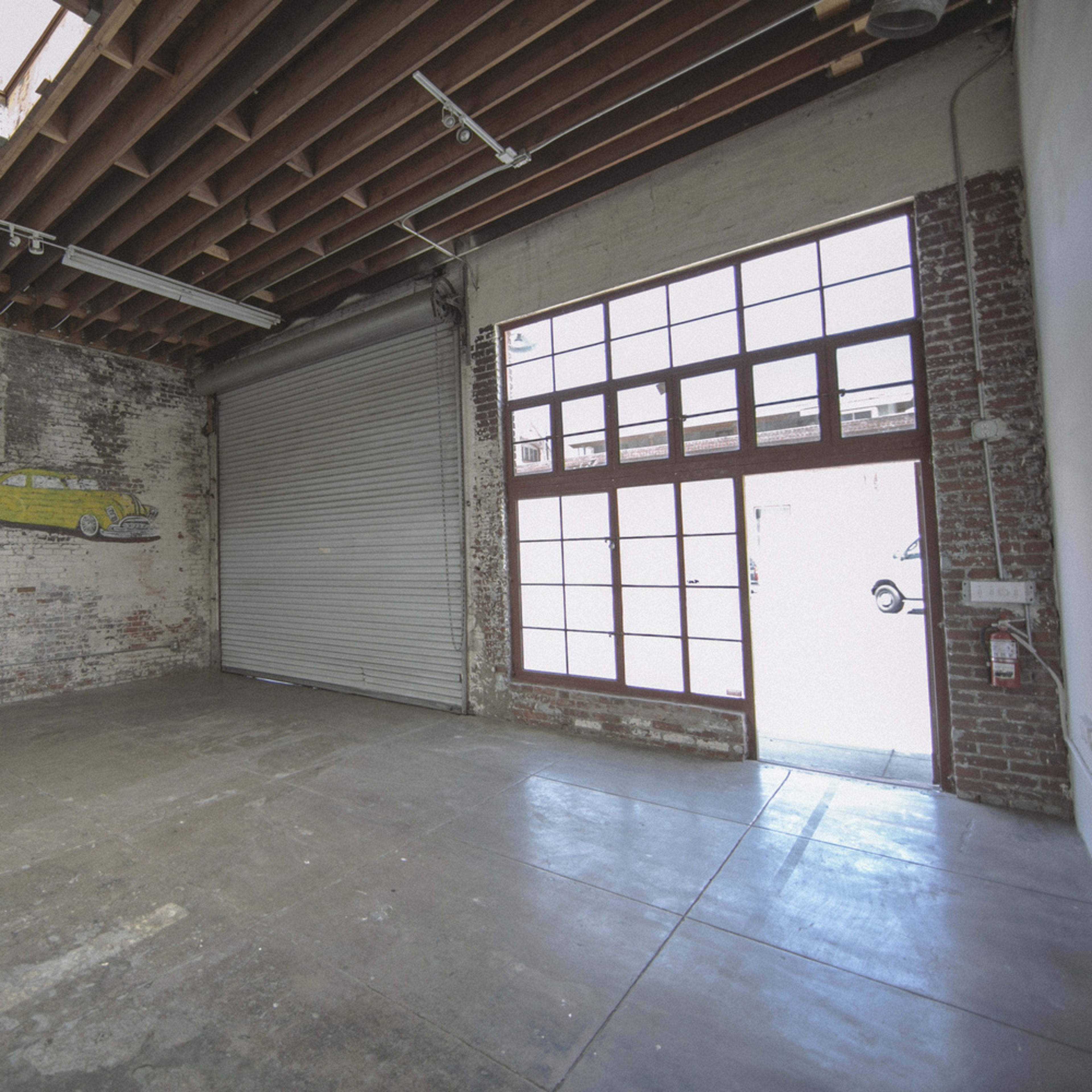 An empty industrial space with a brick wall, a large window with multiple panes, and a roll-up door.