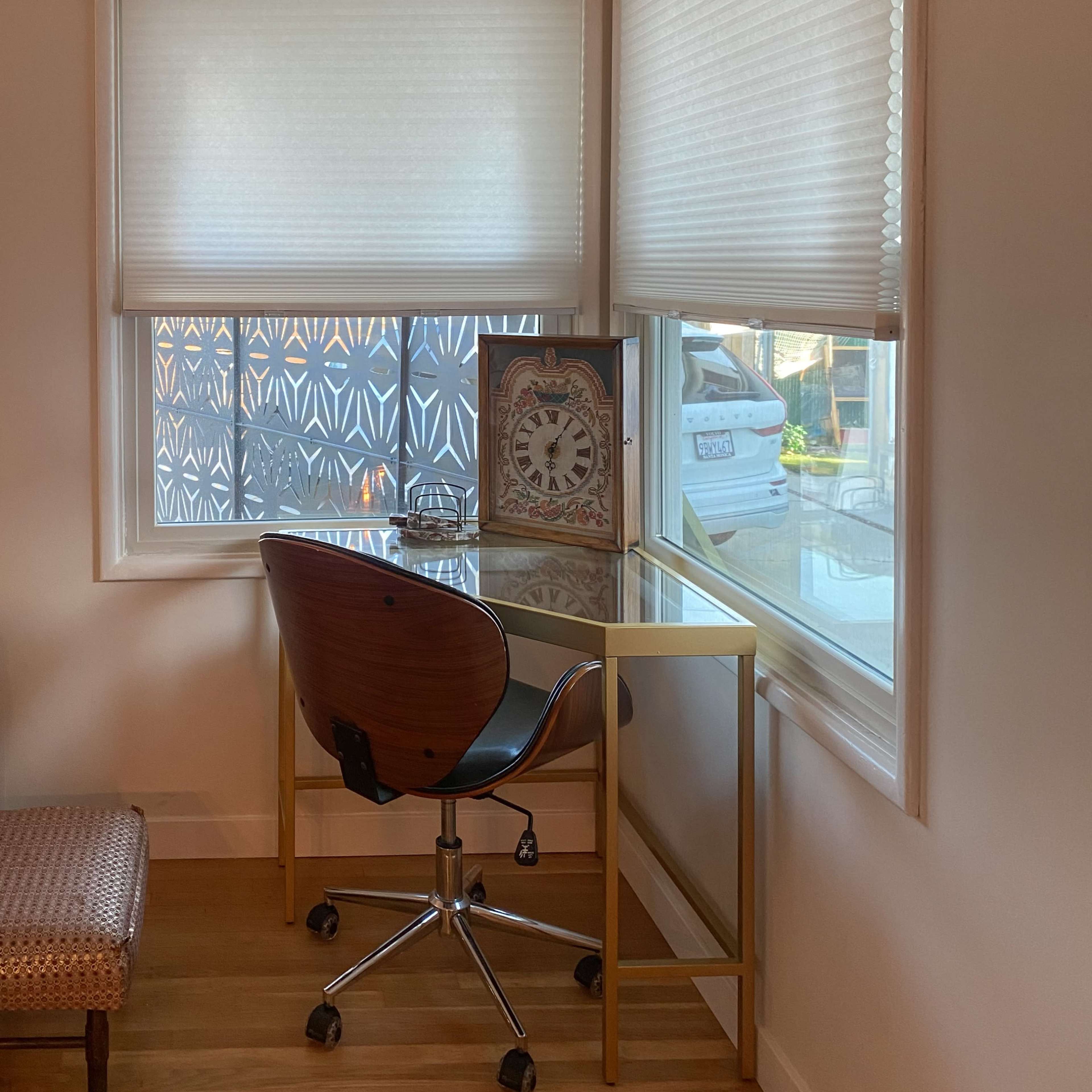 A modern desk with a chair is positioned in a corner near a window, adorned with a clock and illuminated by natural light.