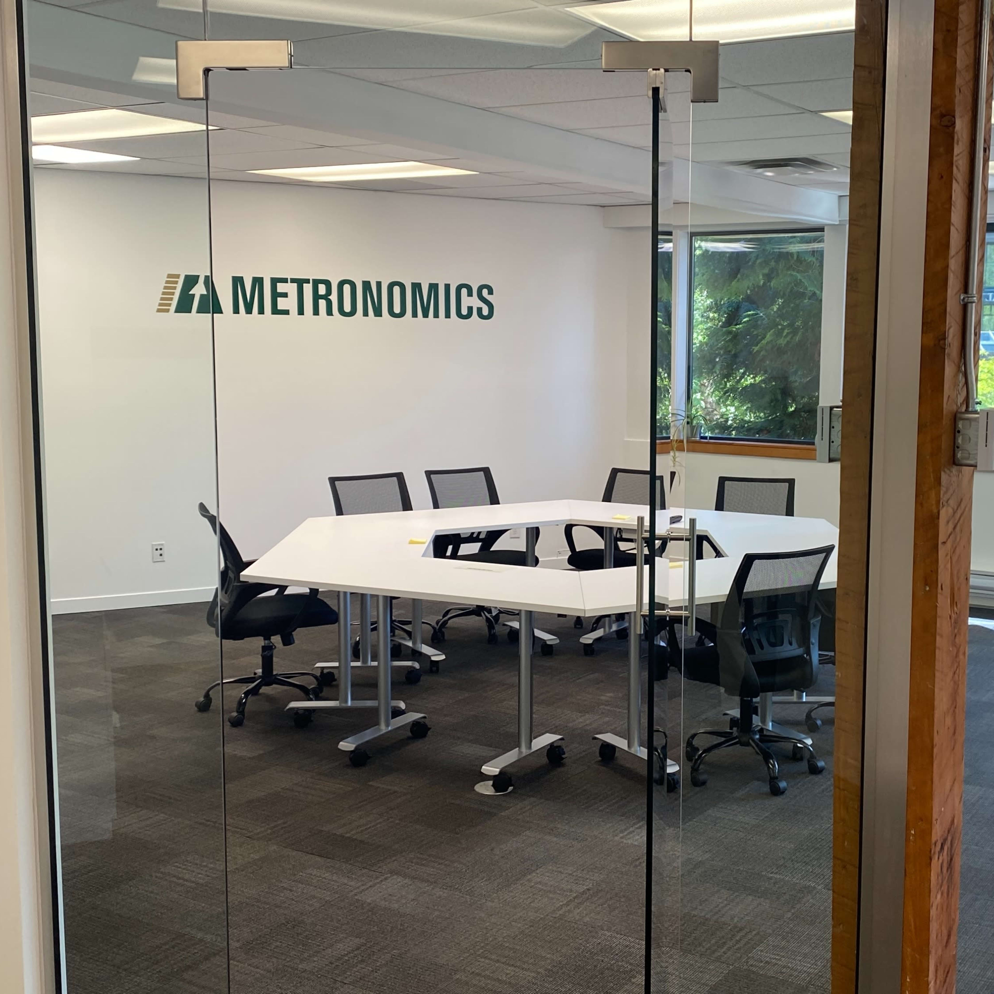 A conference room with a large white table and black chairs is visible through glass doors, featuring the logo of Metronomics on the wall.