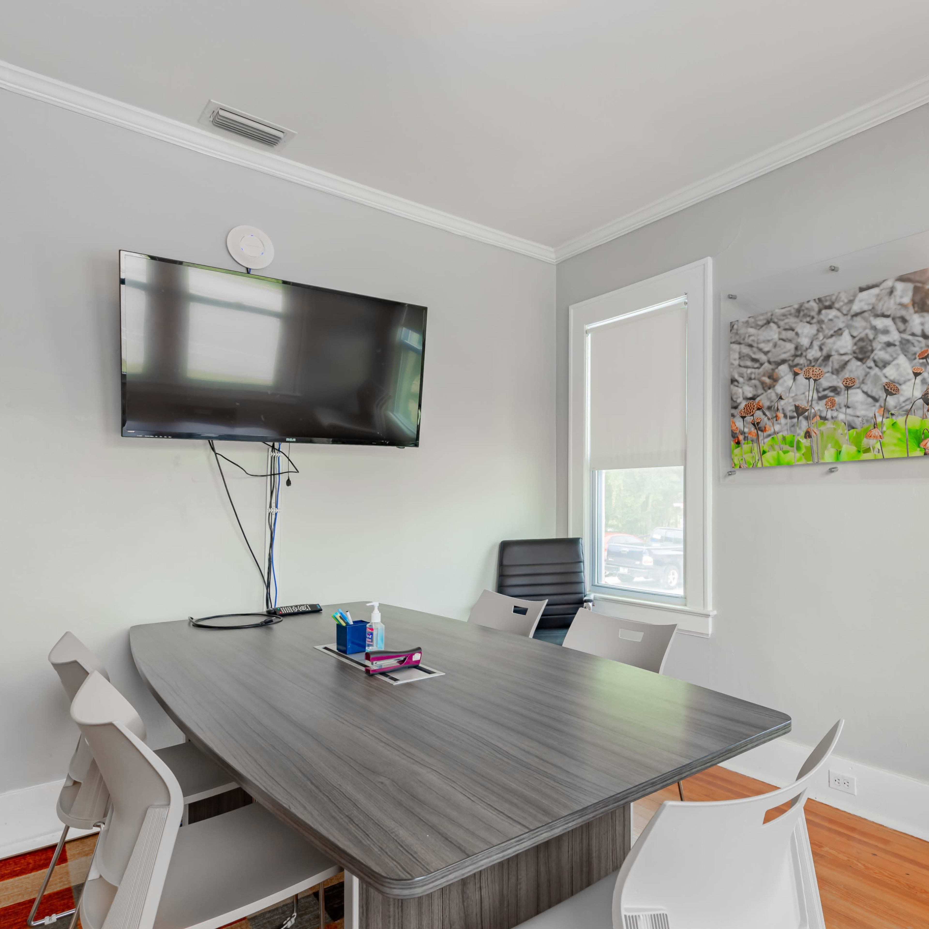 A modern conference room features a large table, comfortable chairs, a wall-mounted television, and a decorative wall panel with stones and greenery.