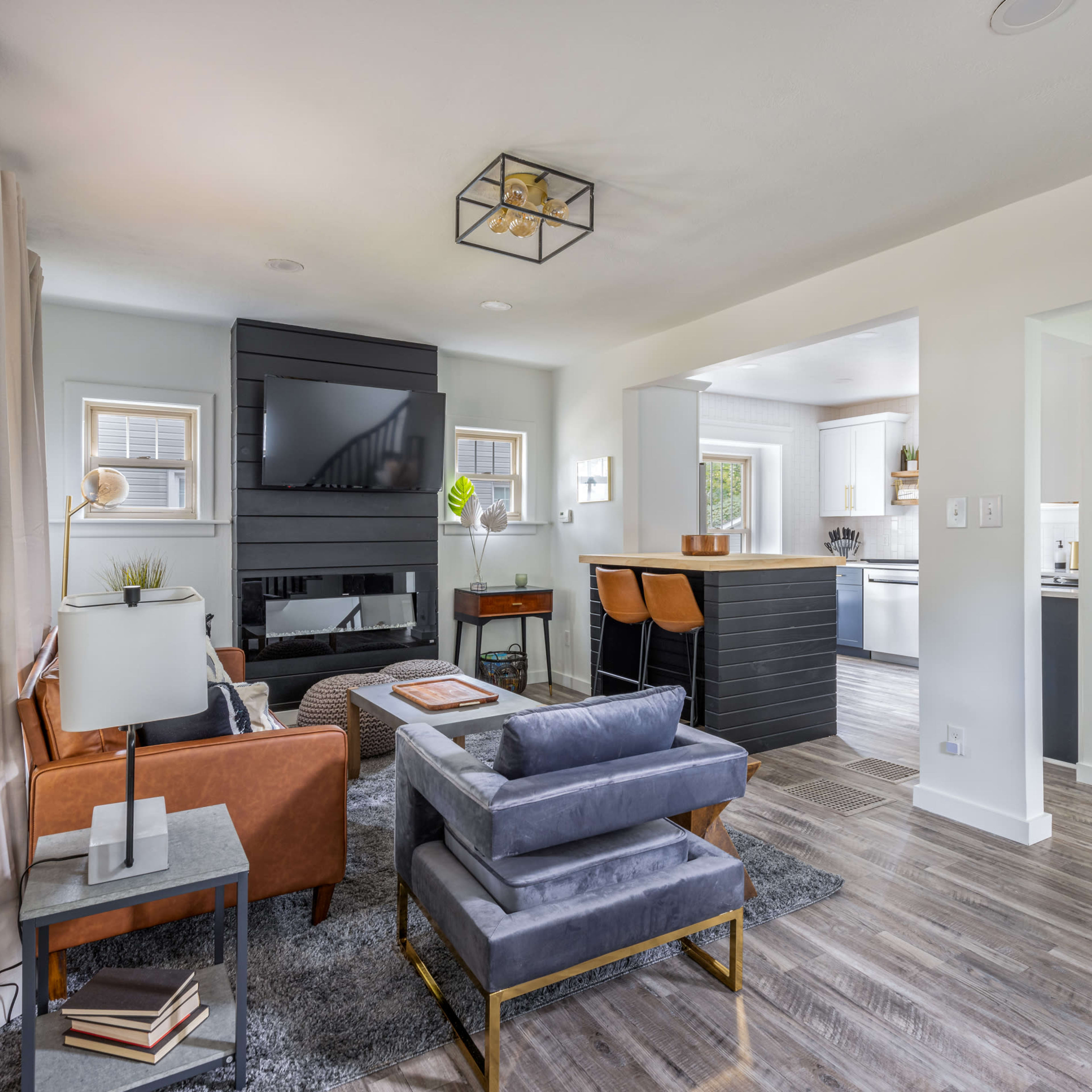 A modern living room with a leather sofa, a gray rug, and a black fireplace, connected to a kitchen area.