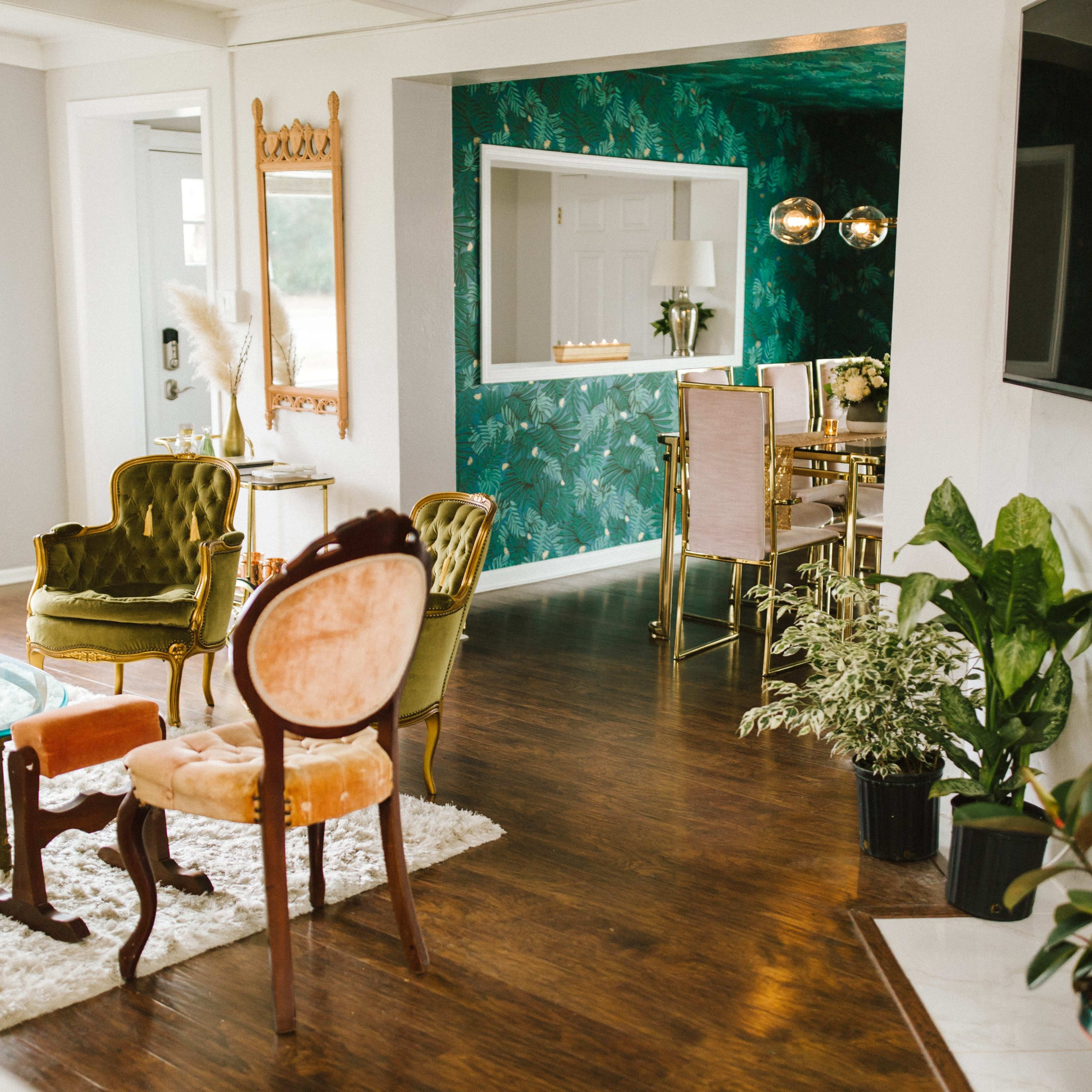 A bright, modern living space with a mix of seating and decorative elements, featuring a green accent wall and a dining area visible in the background.