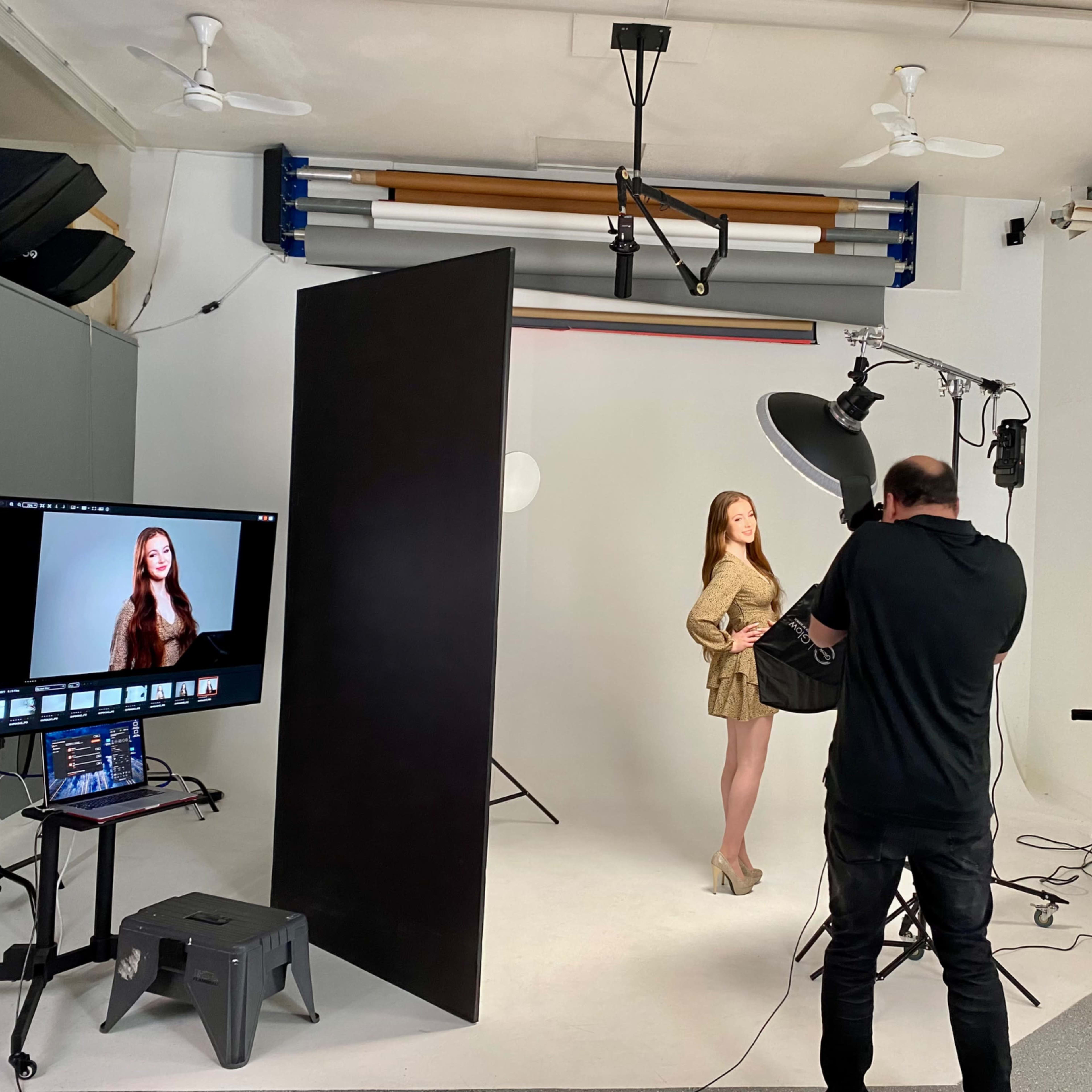 A photographer captures a model posing in a studio setup with backdrop and lighting equipment.