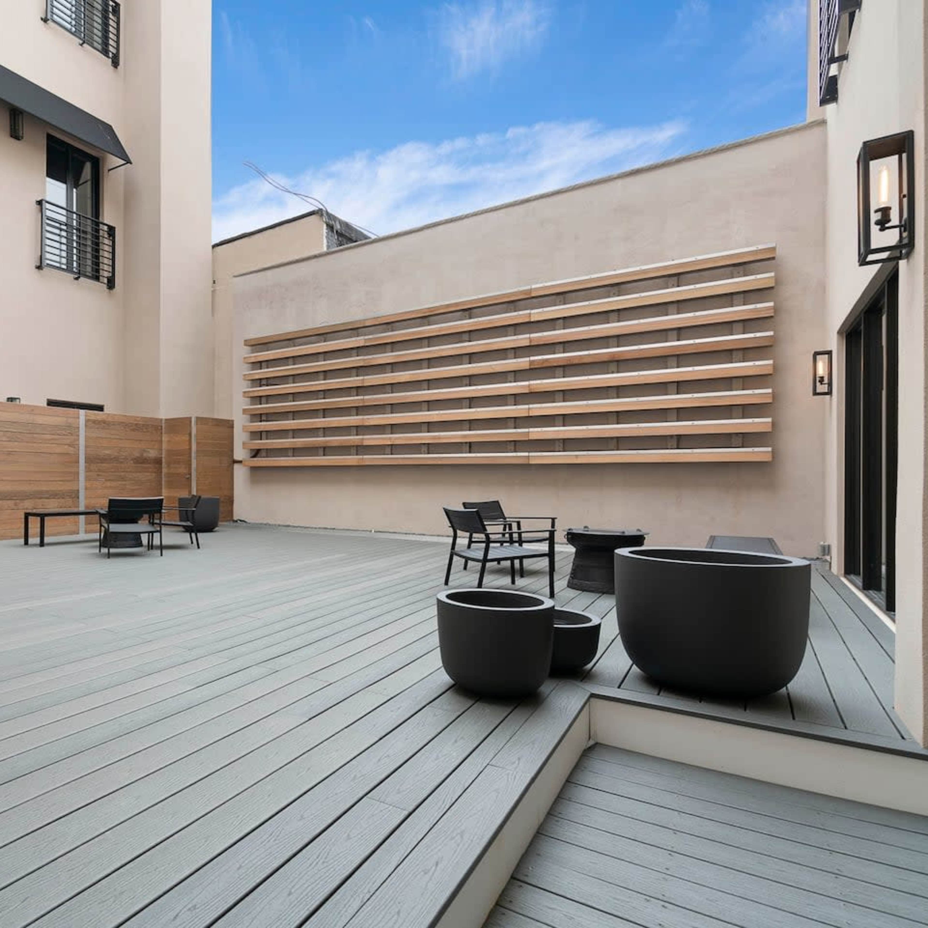 A spacious outdoor patio area with wooden fencing, several black chairs, and planters on a light gray deck.