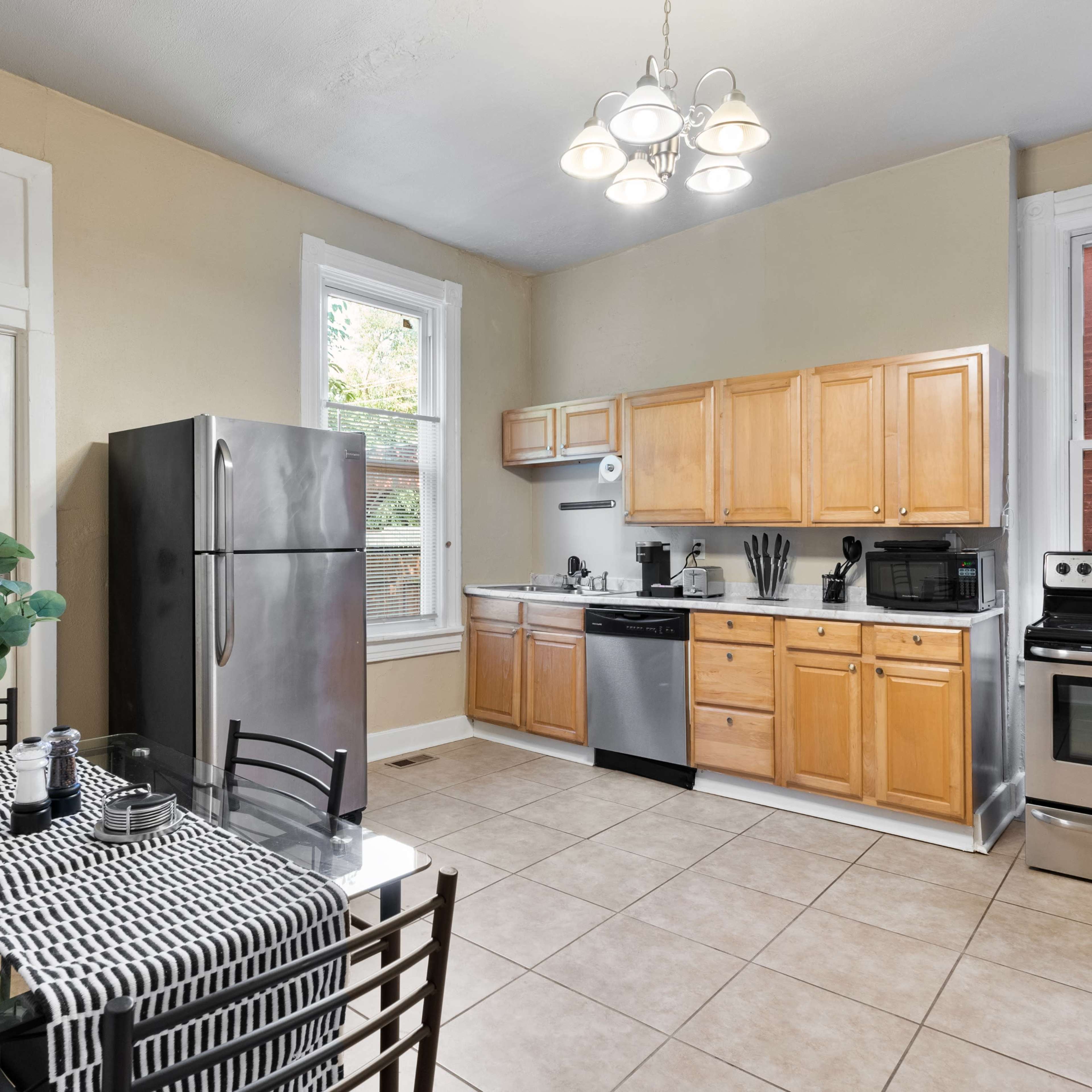 A kitchen with wooden cabinets, a stainless steel refrigerator, and a dining table set with a black and white table runner.