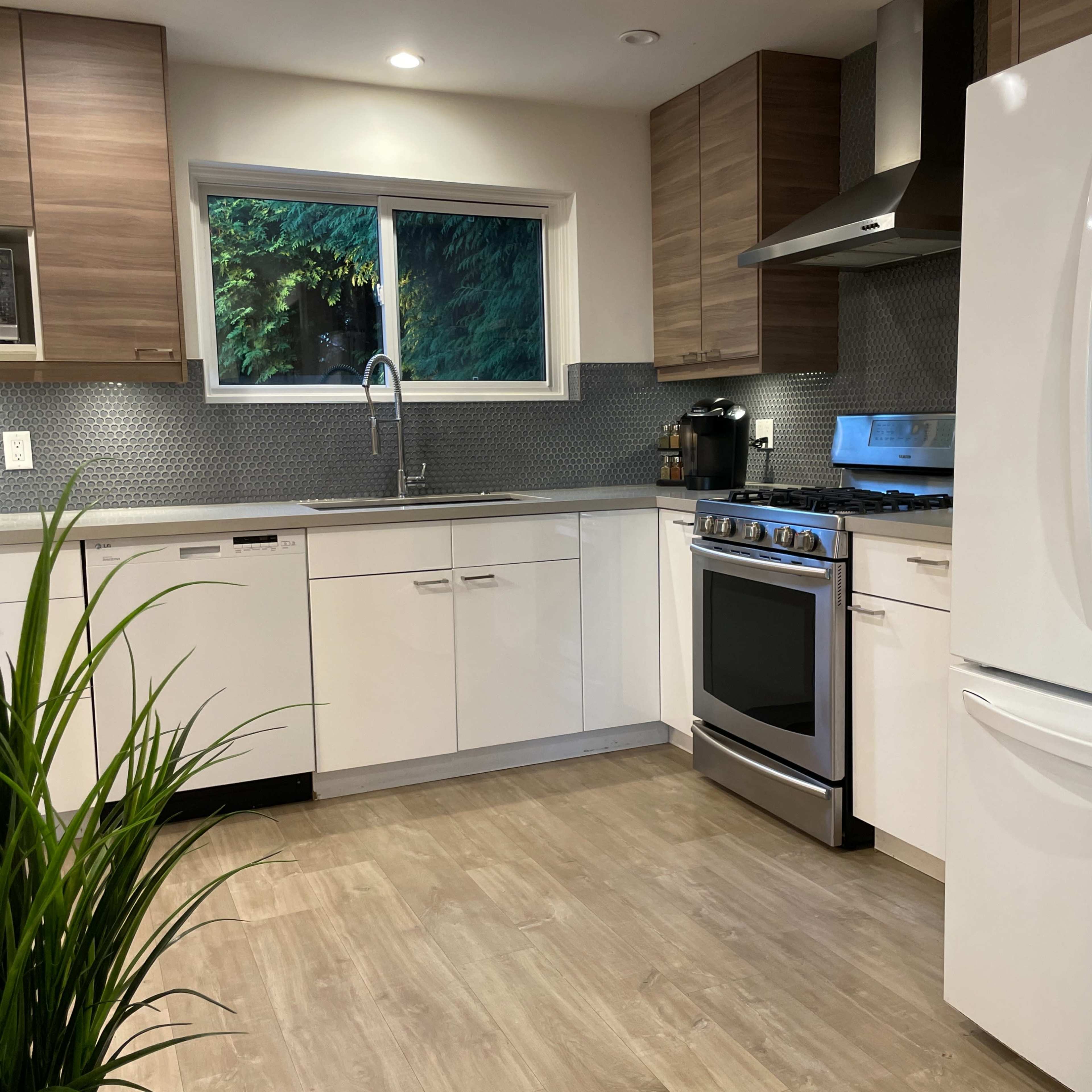 A modern kitchen featuring light wood cabinetry, stainless steel appliances, and a window overlooking greenery.