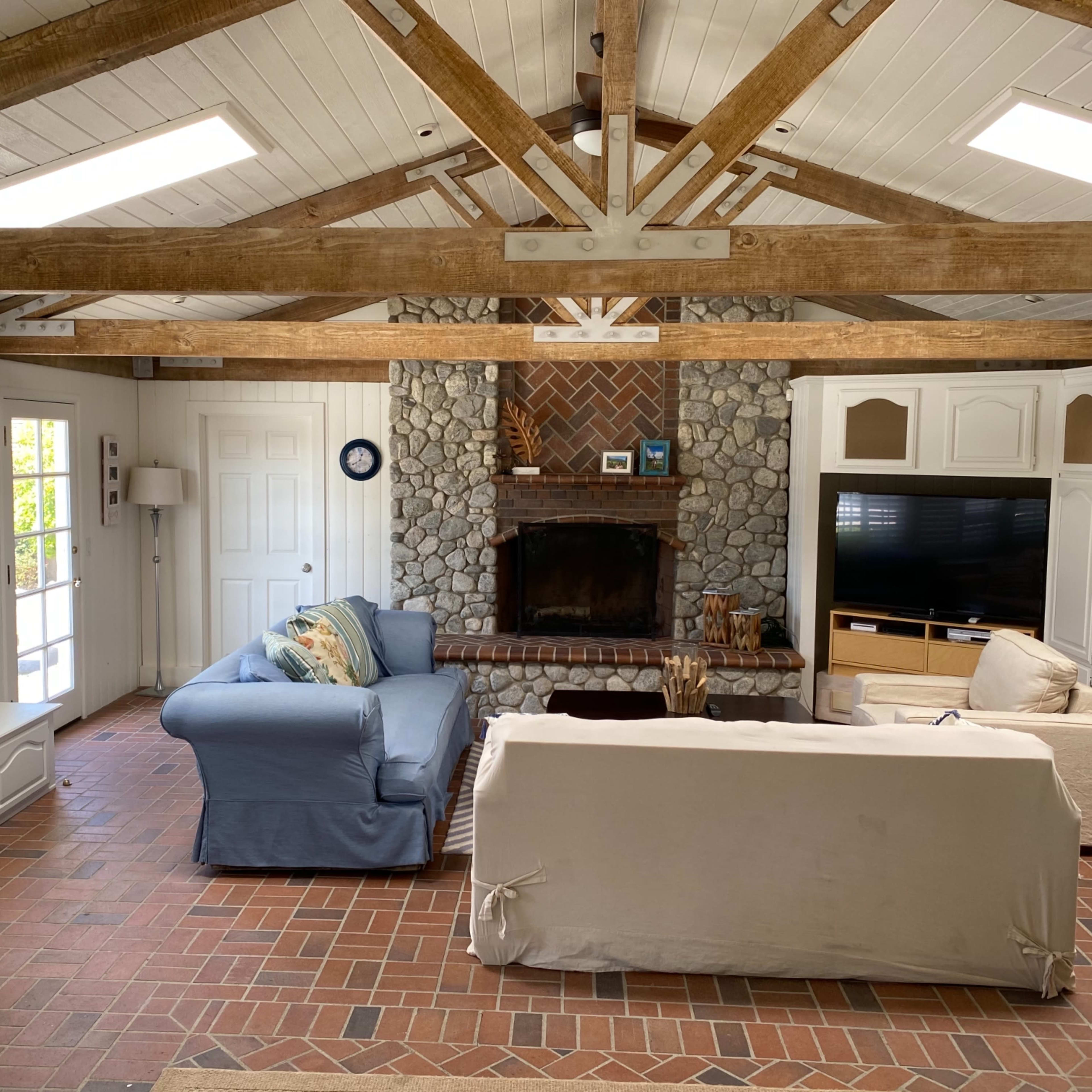 A living room with a stone fireplace, exposed wooden beams, and two sofas facing each other.