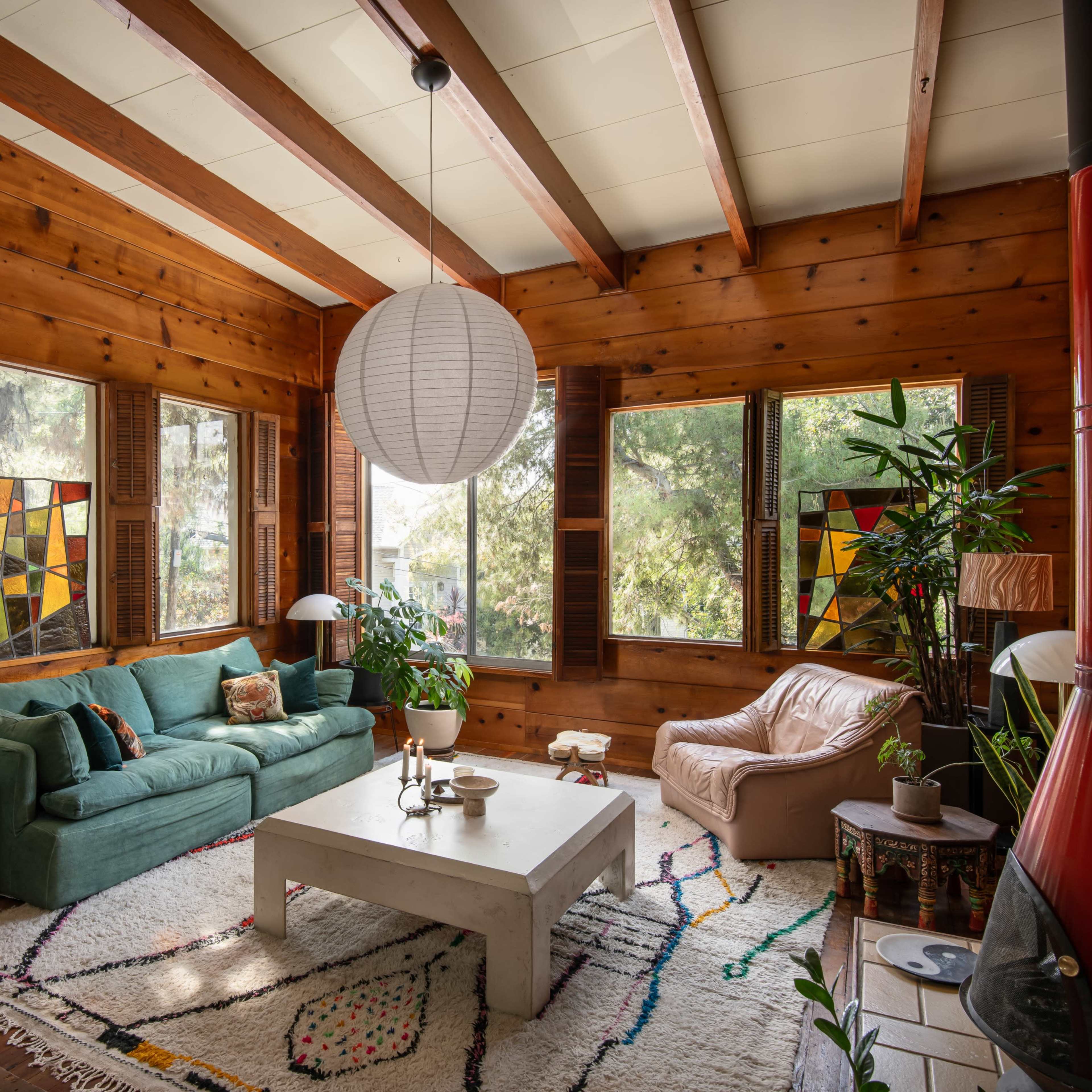 A wooden-paneled living room featuring a green sofa, a white coffee table, and large windows with colorful stained glass.