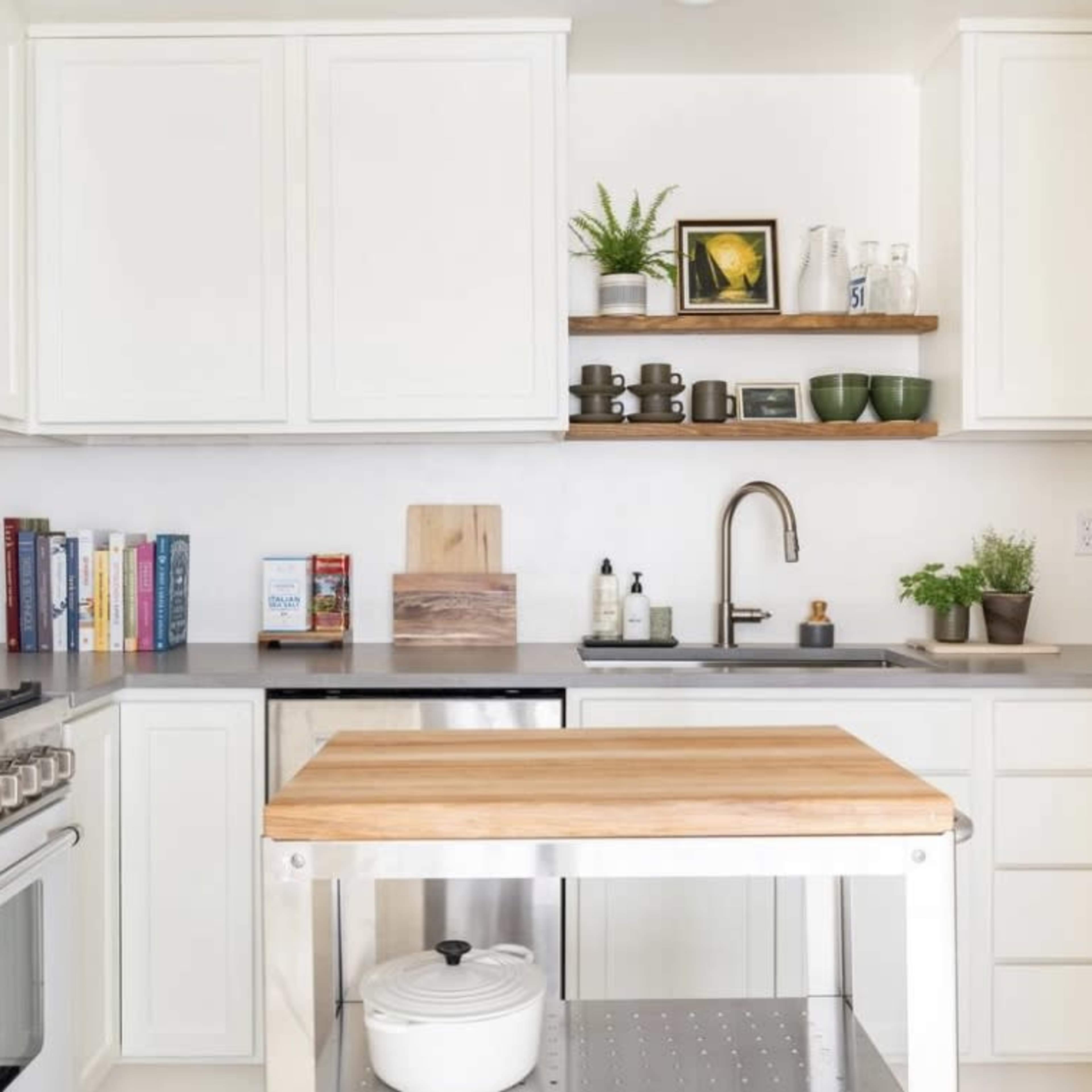 The kitchen features white cabinetry, a stainless steel refrigerator, a wooden countertop island, and various kitchen accessories arranged neatly on shelves and countertops.