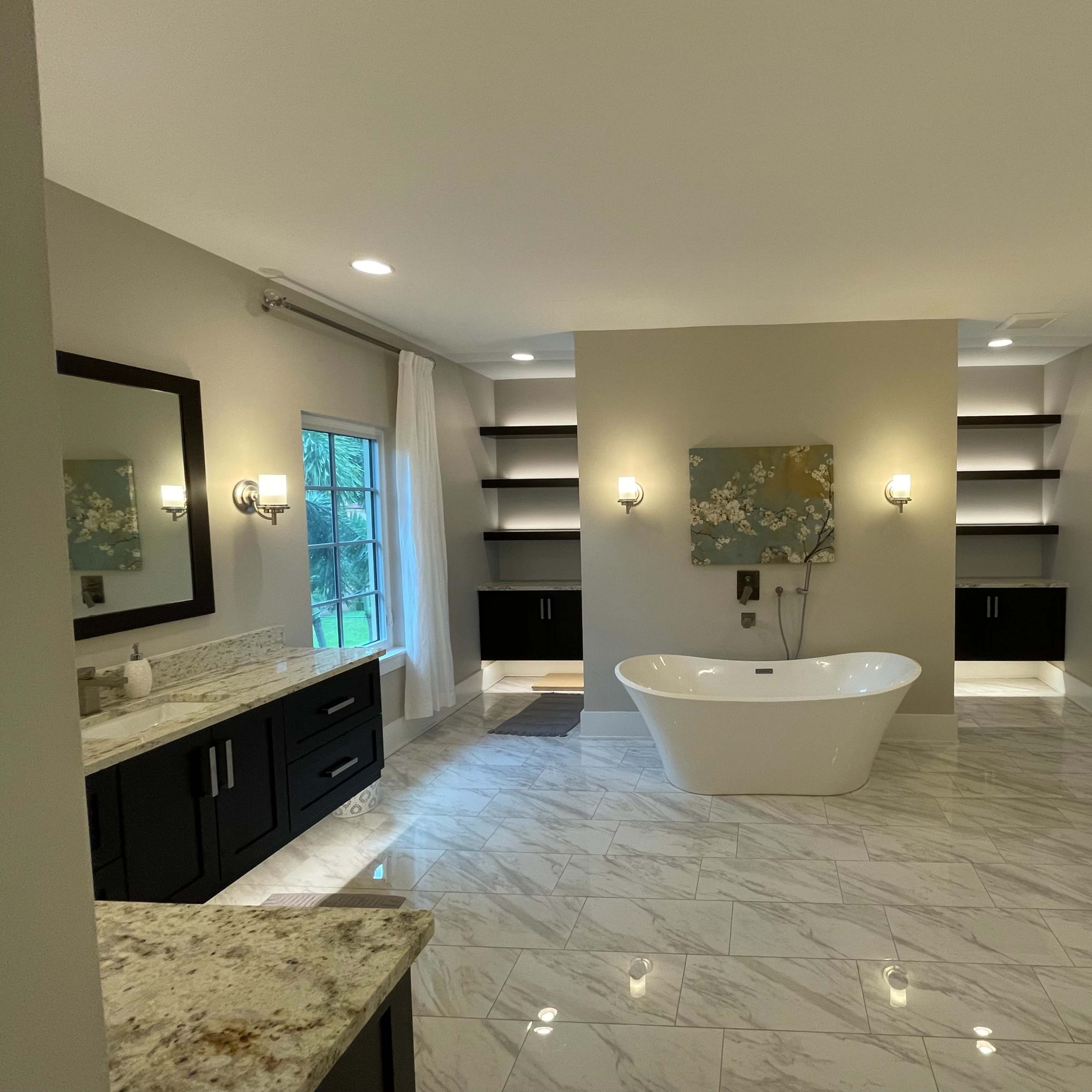 A spacious modern bathroom featuring a freestanding bathtub, dual vanities with dark cabinets, and a marble floor.