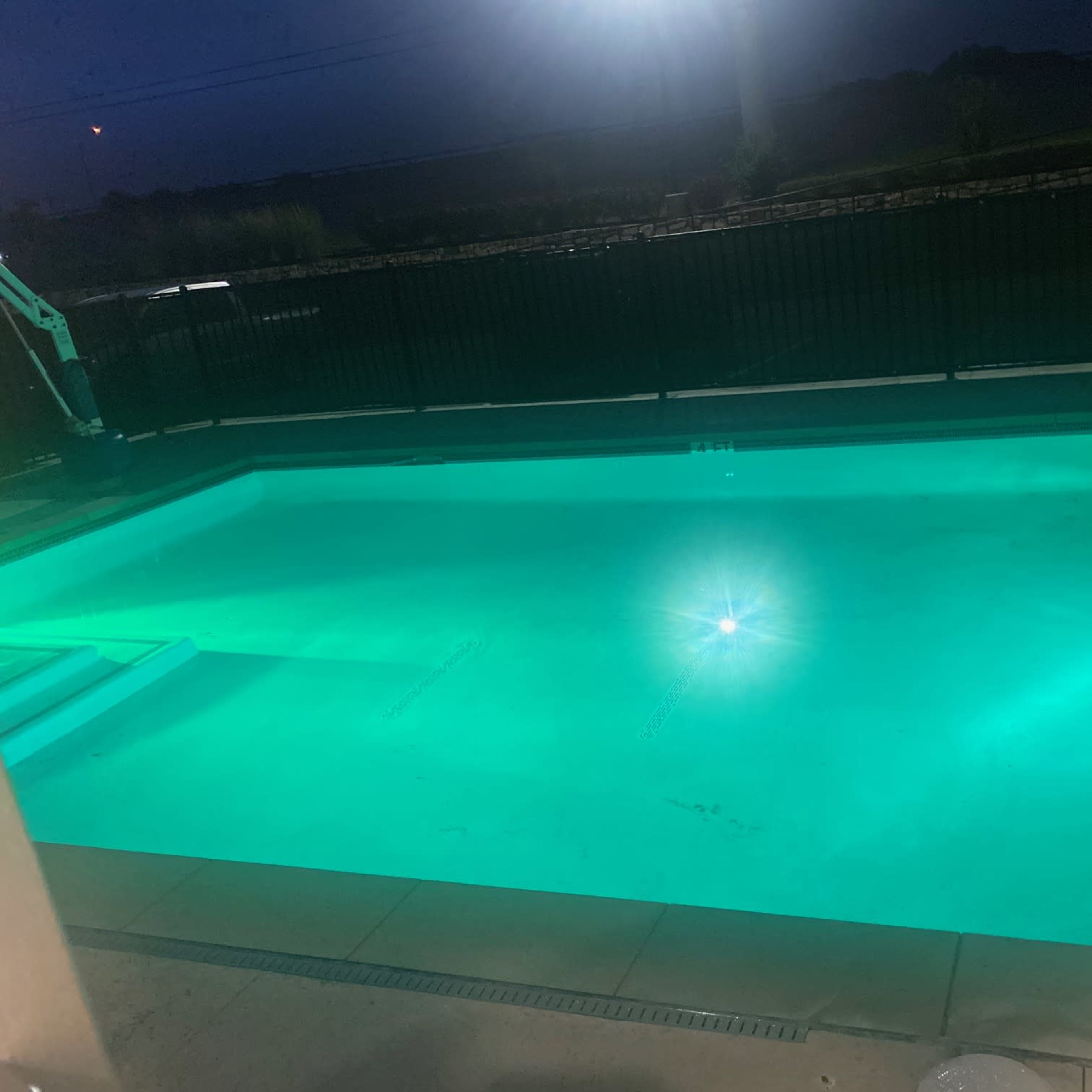 A well-lit swimming pool glows turquoise under the night sky.