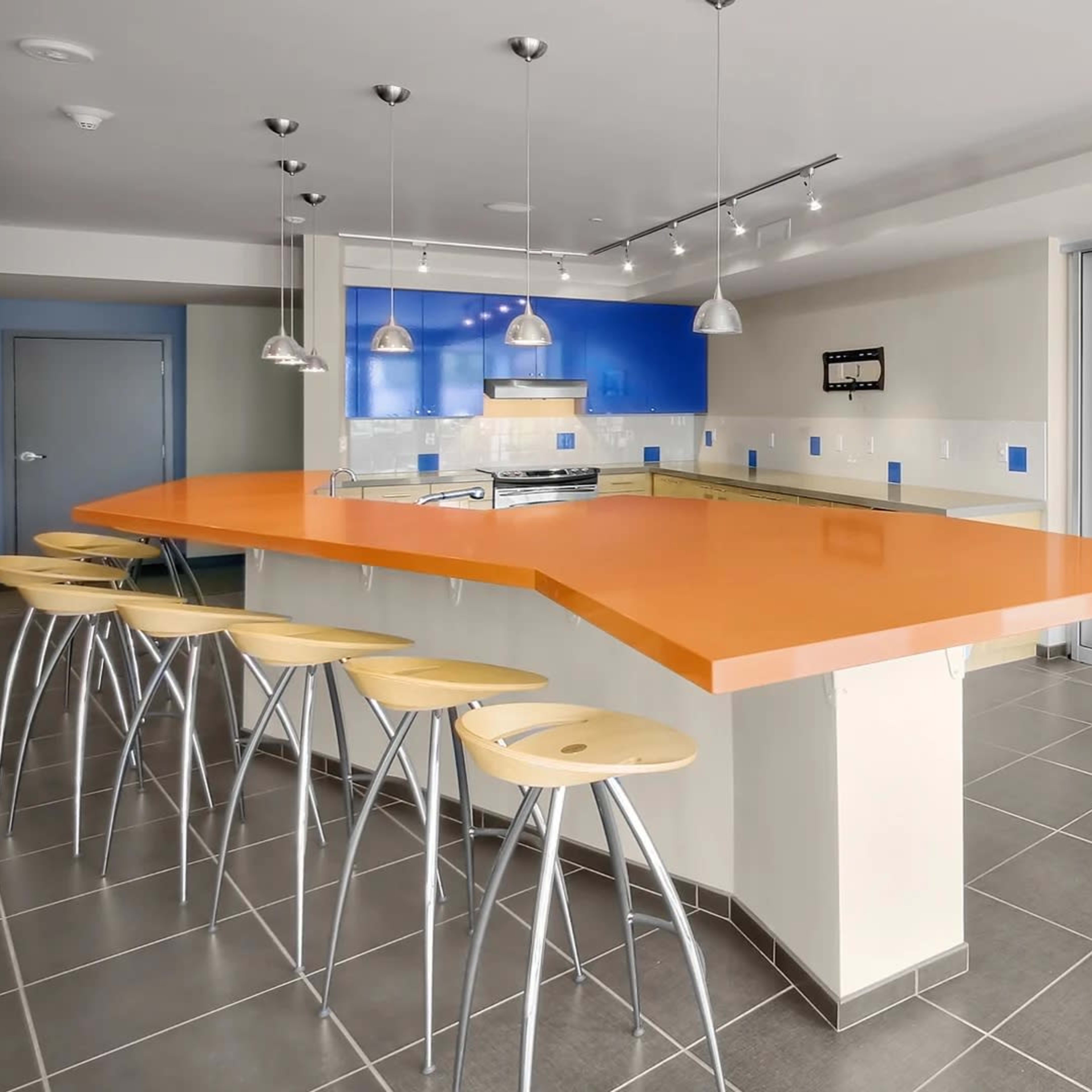 A modern kitchen features an orange countertop with bar stools and a view of a separate room containing a pool table.