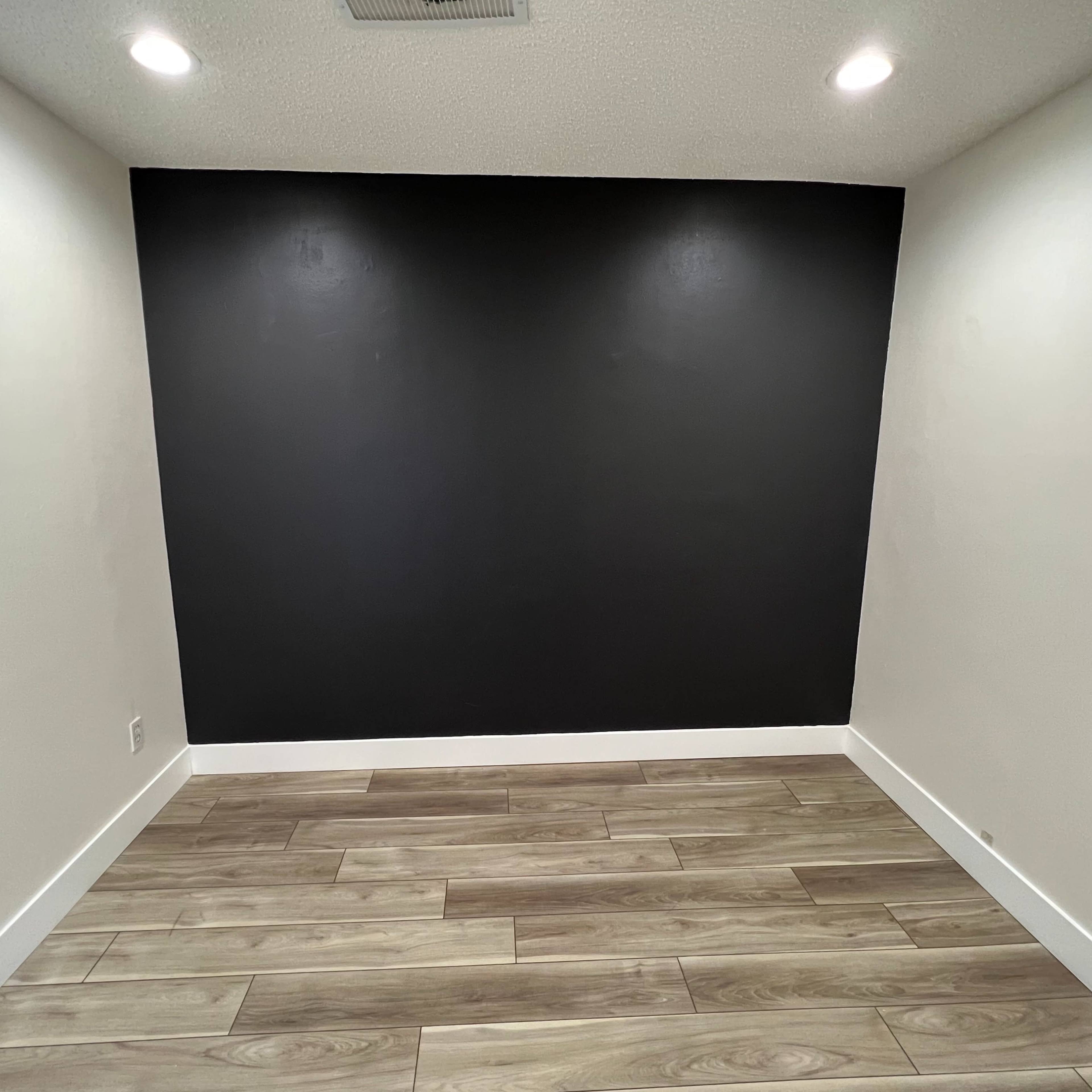 A small, empty room with a black accent wall and light-colored wood flooring.