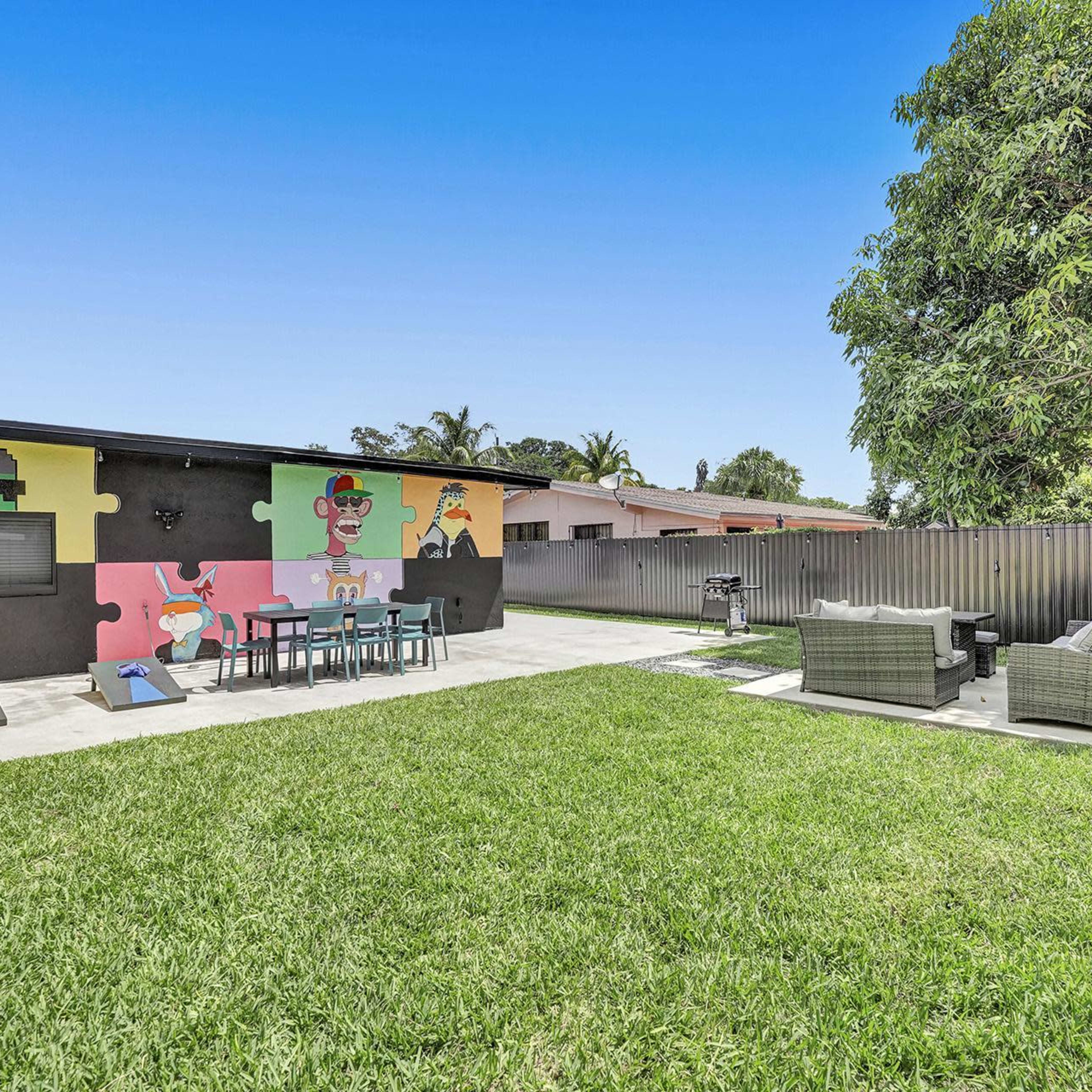 A backyard with a grassy area, a patio featuring outdoor furniture, and a colorful mural on one wall.