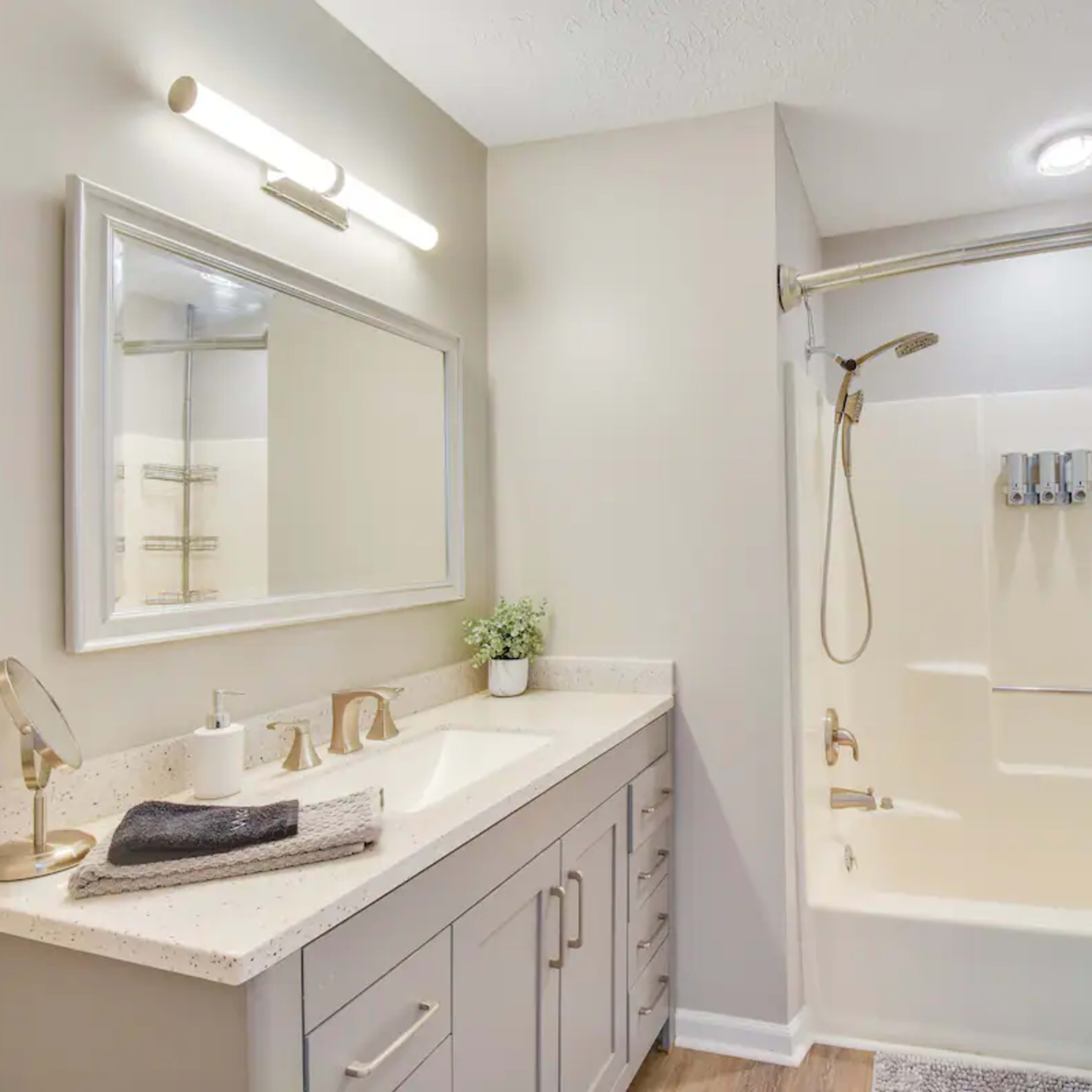 A bathroom features a shower-tub combination, a vanity with a mirror, and soft lighting.