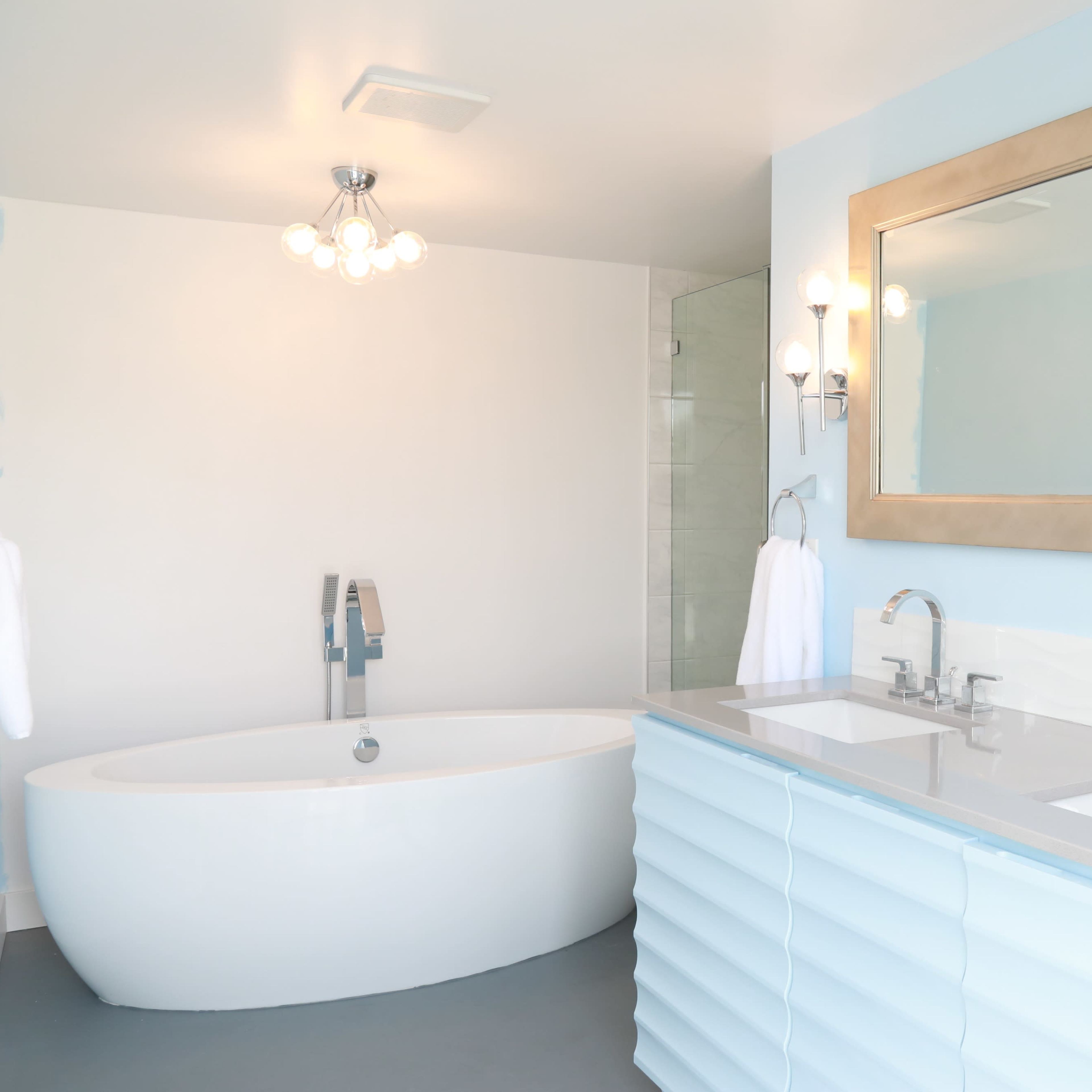 A modern bathroom features a freestanding white tub, dual sinks with a light blue vanity, and a large mirror above the sinks.