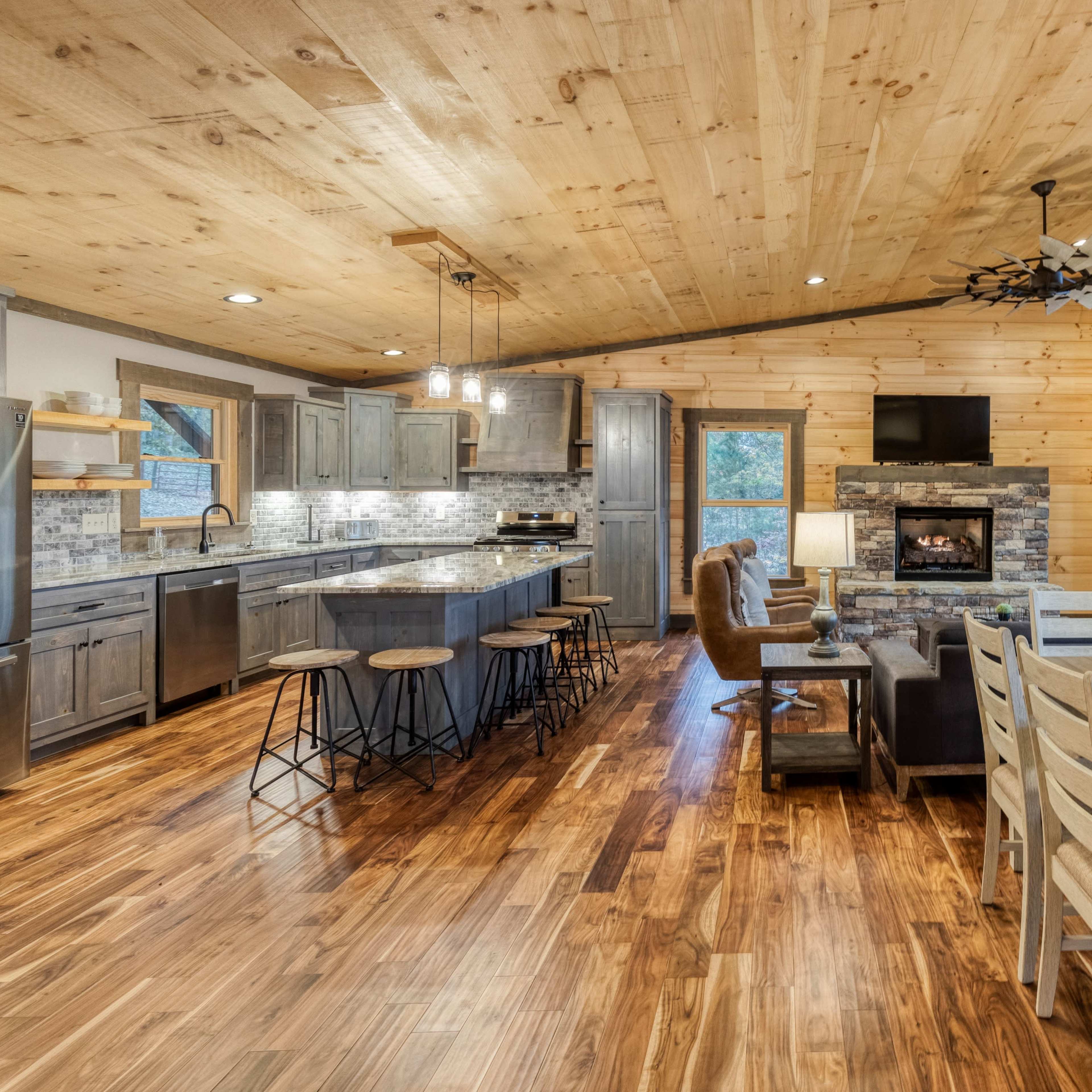 A modern, open-concept kitchen and dining area in a cabin-style interior with wooden walls and flooring.