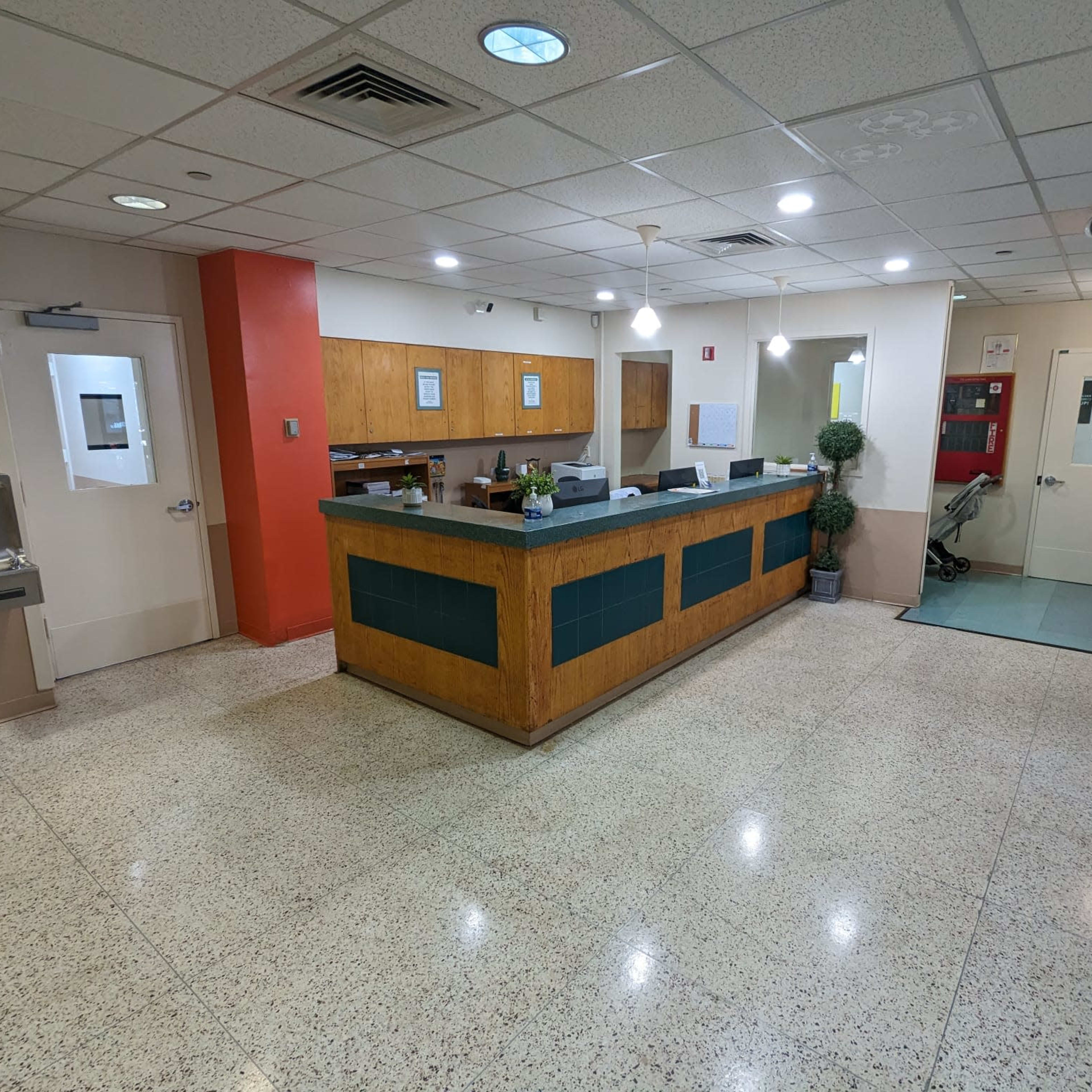 A reception area with a wooden front desk, a tiled floor, and various office equipment in a well-lit space.