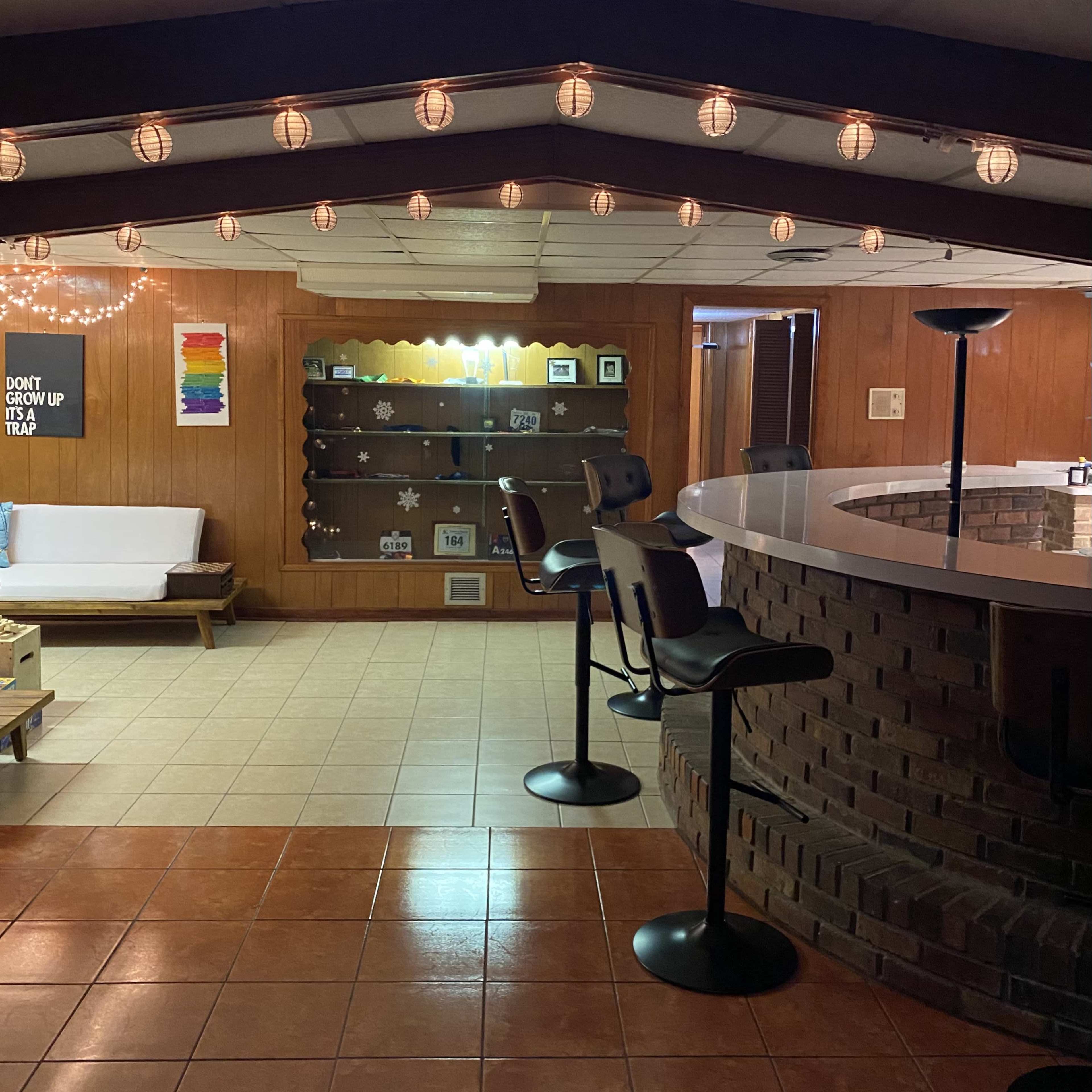 A basement room with a bar area, seating, and string lights illuminating the ceiling.