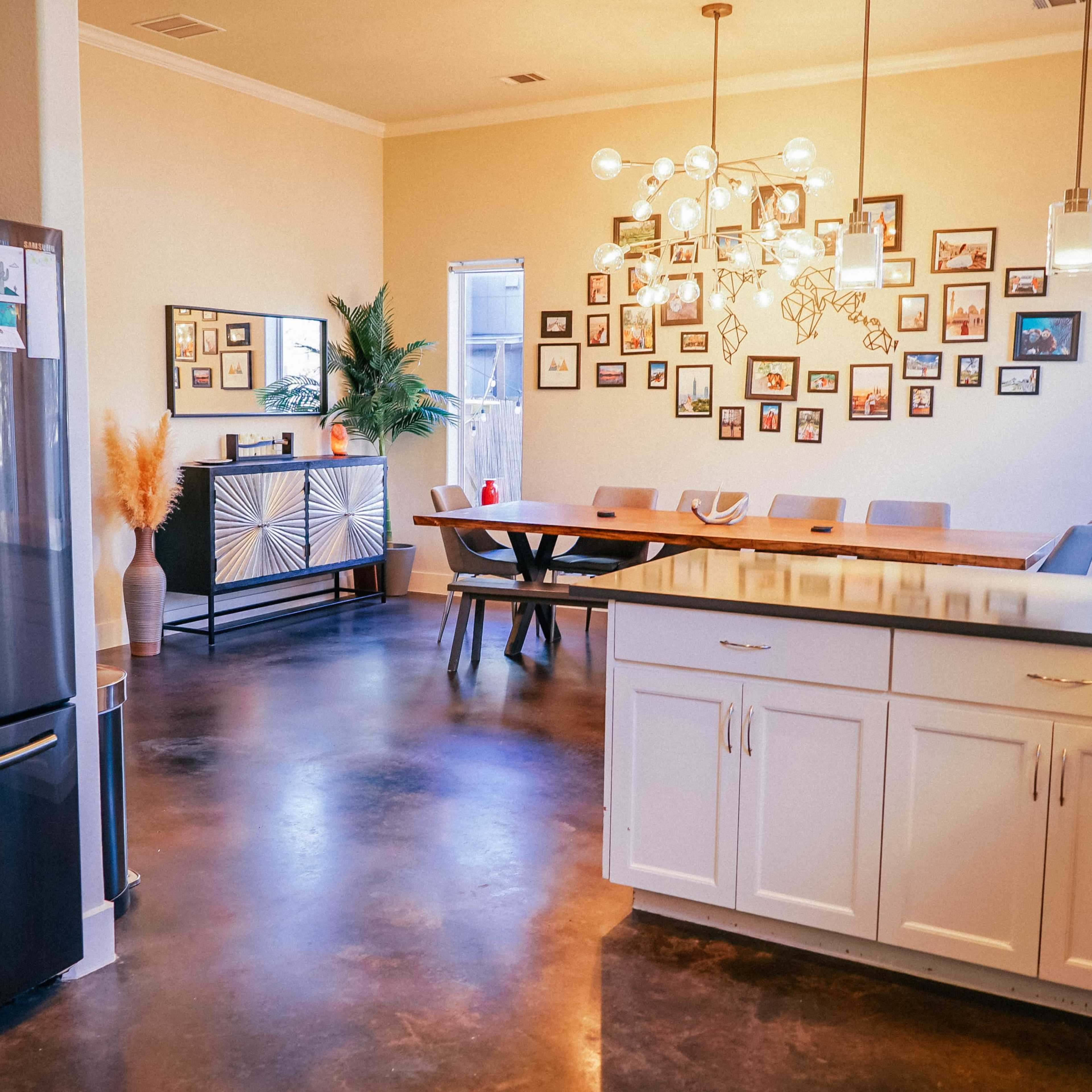 A modern kitchen and dining area with a stainless steel refrigerator, a large wooden dining table, and walls decorated with a collage of framed pictures.