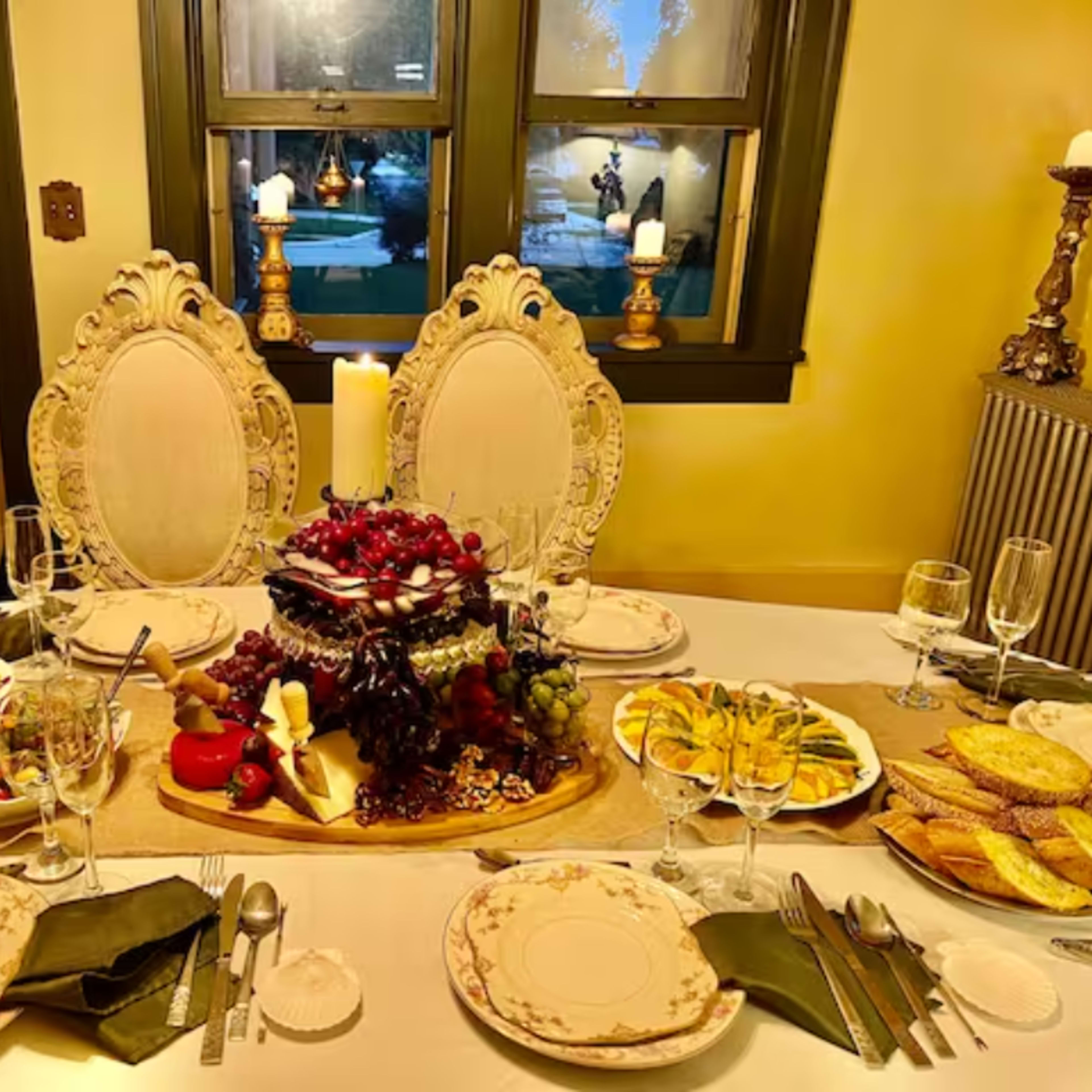 A beautifully set dining table features an array of dishes including salads, fruits, cheese, and bread, surrounded by elegant tableware and candlelight.