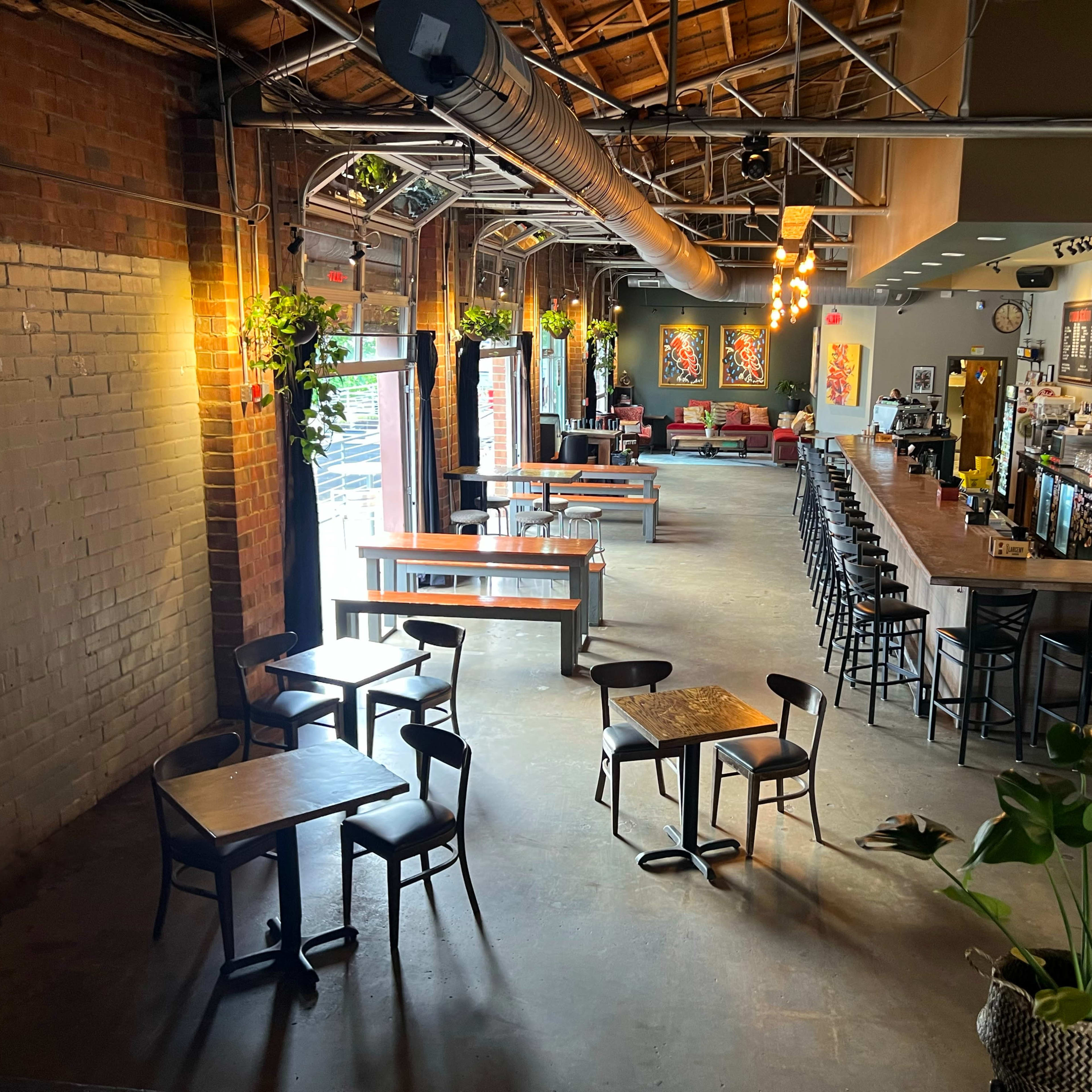 An expansive bar and dining space with wooden tables and chairs, a long bar counter, and large windows that open to an outdoor area.